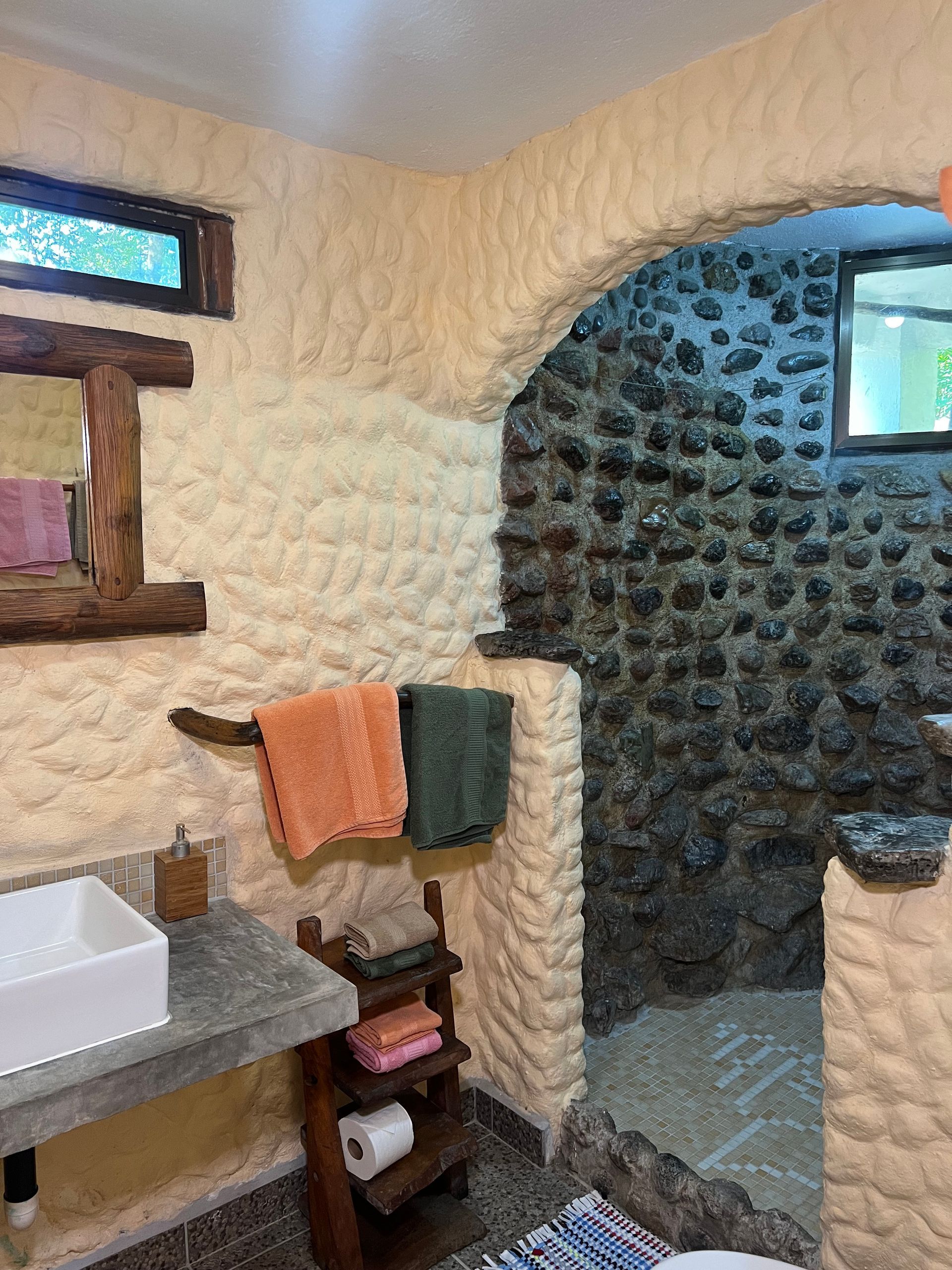 A bathroom with a sink , mirror , towels and a stone wall.