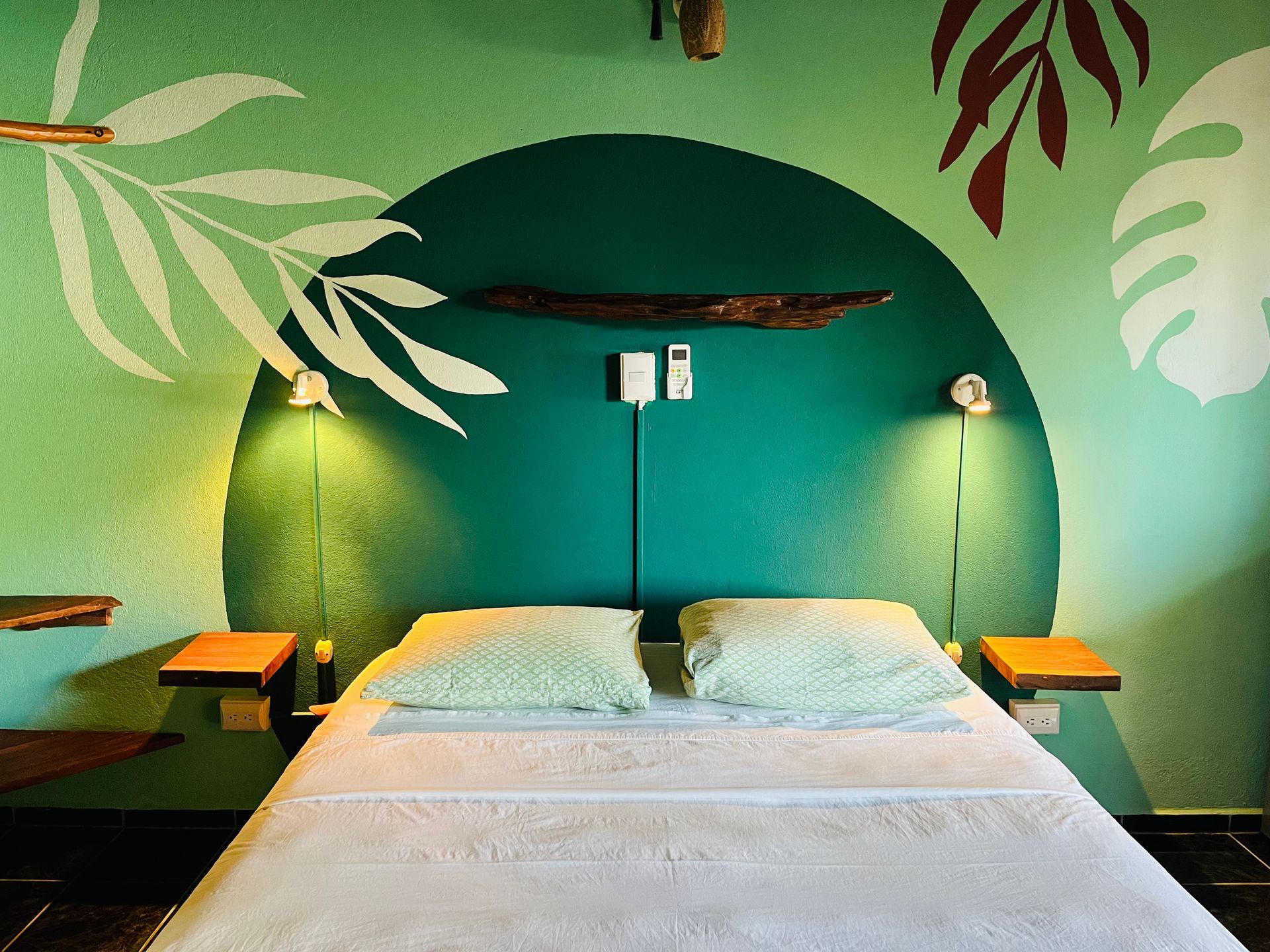 A bedroom with a bed and a green wall with leaves painted on it