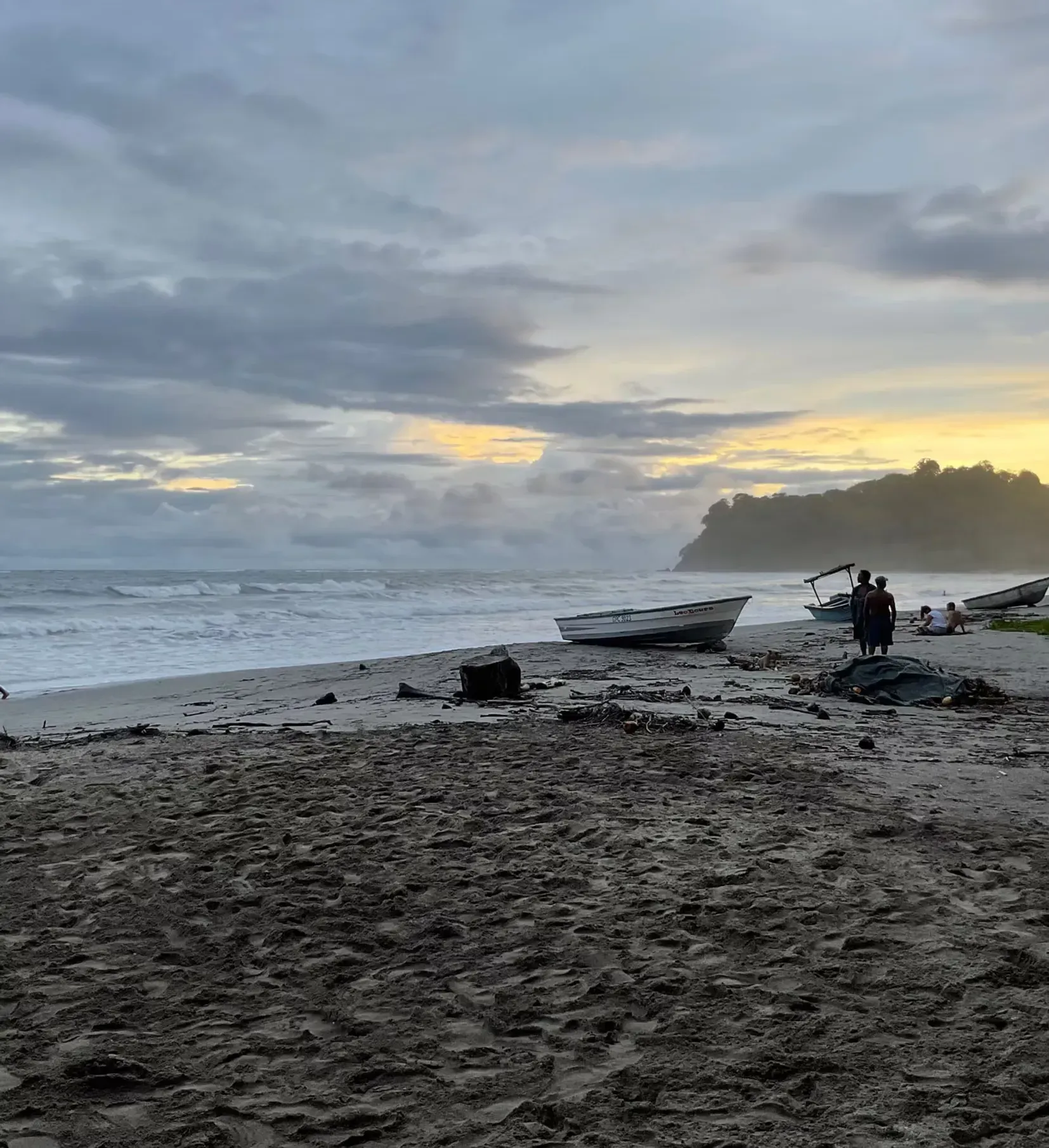 A group of people standing on a beach with boats in the background