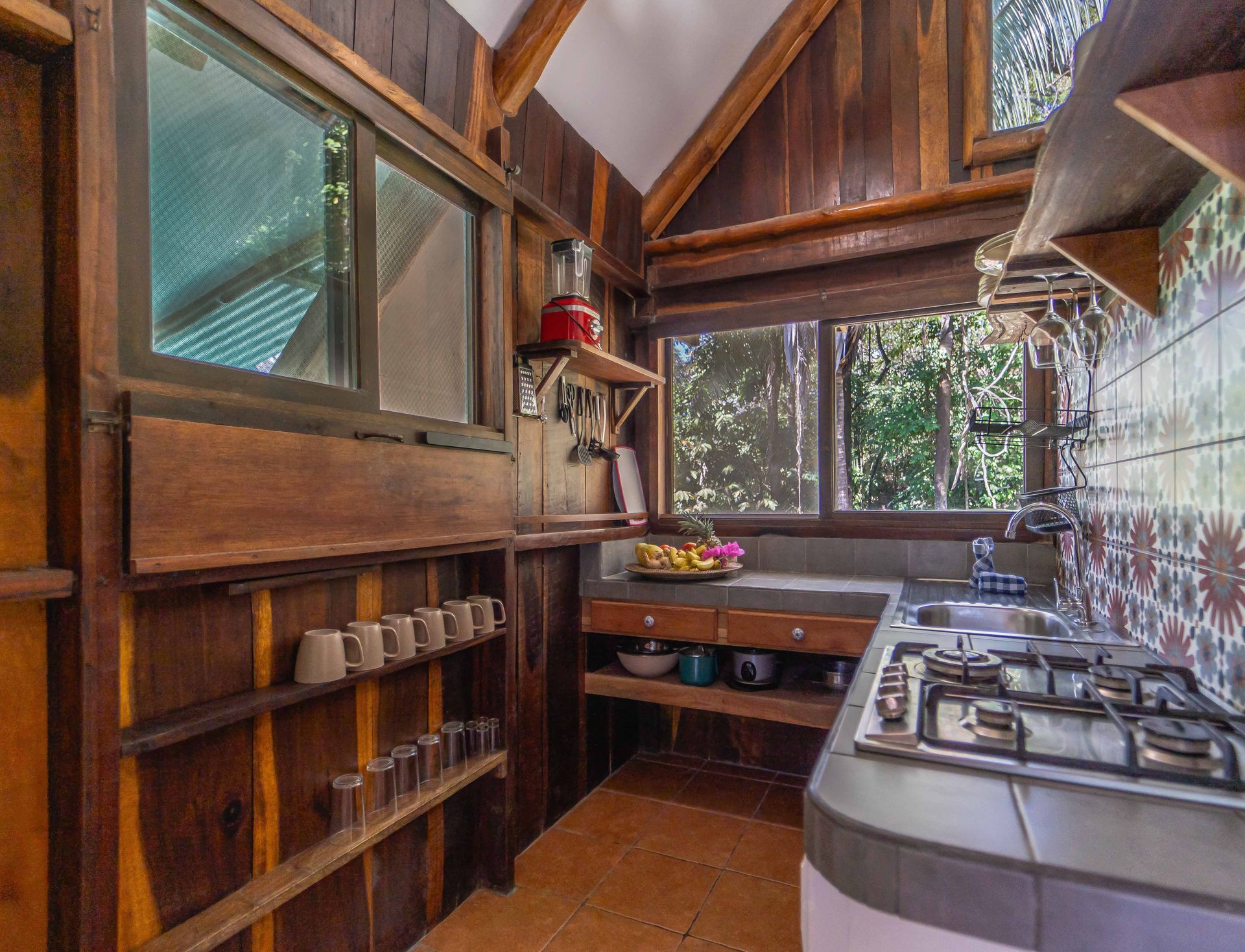 A kitchen with a stove , sink , and lots of windows.