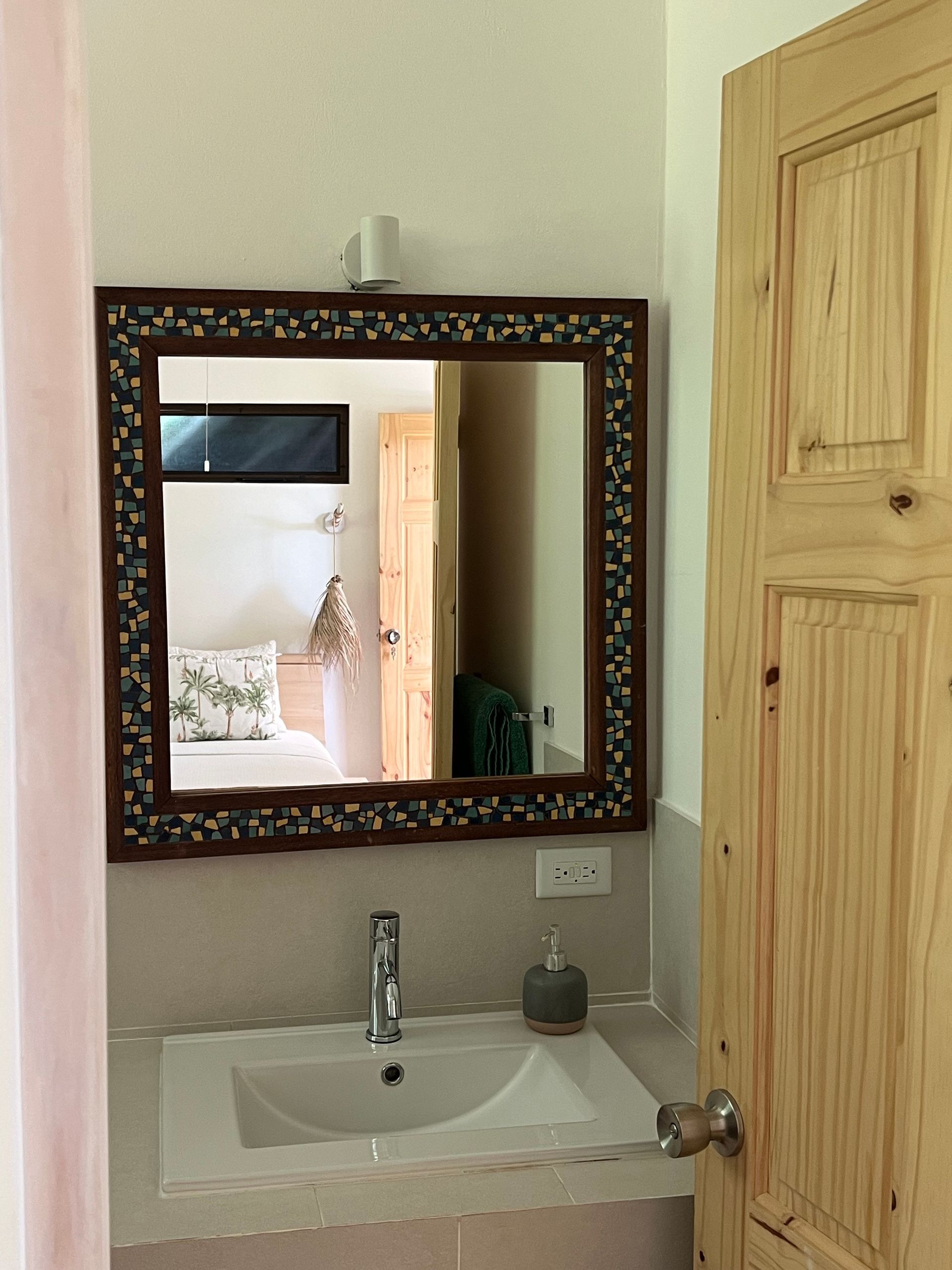 A bathroom with a sink , mirror and wooden door.