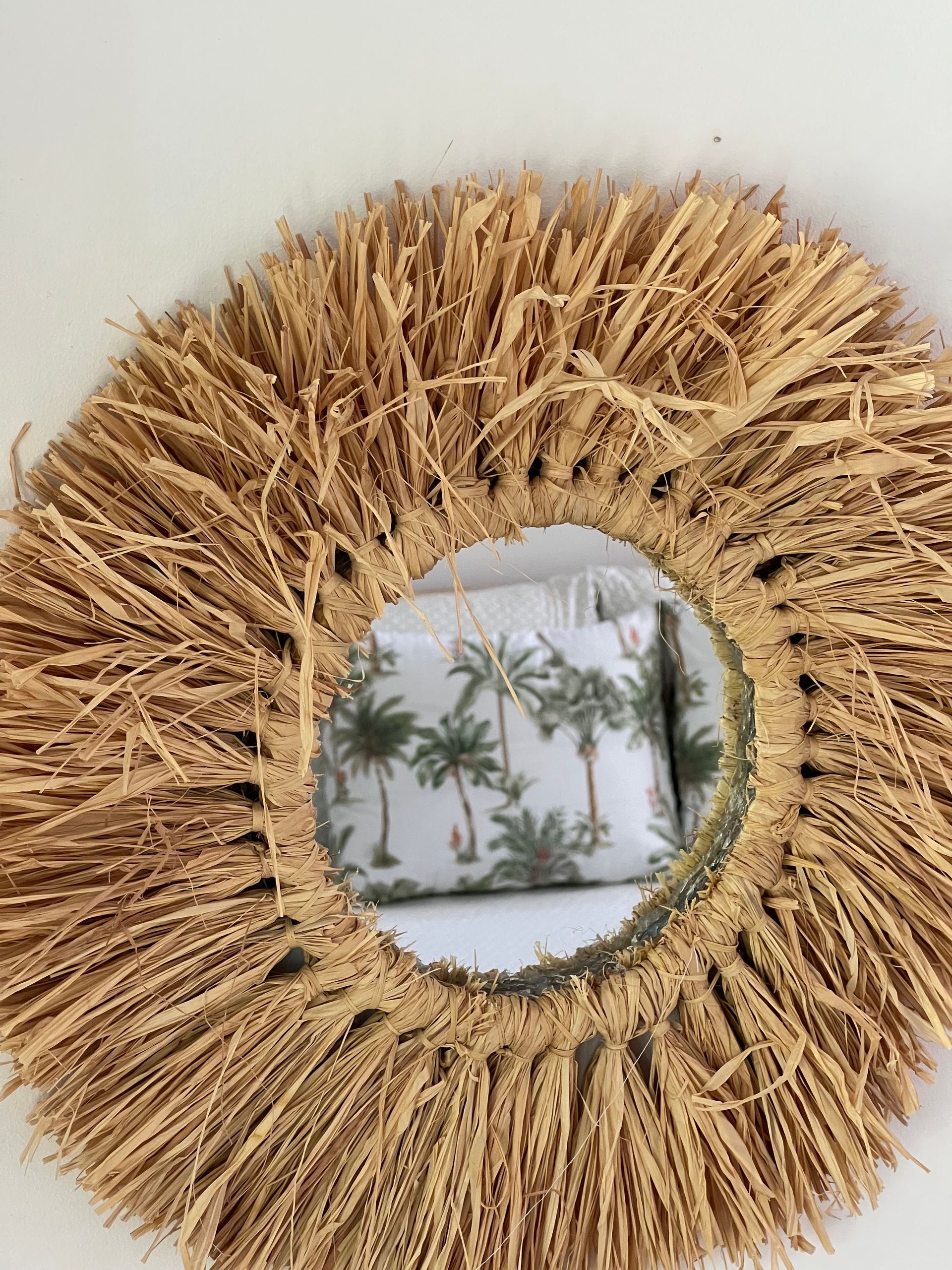 A round mirror with a straw frame is hanging on a wall.