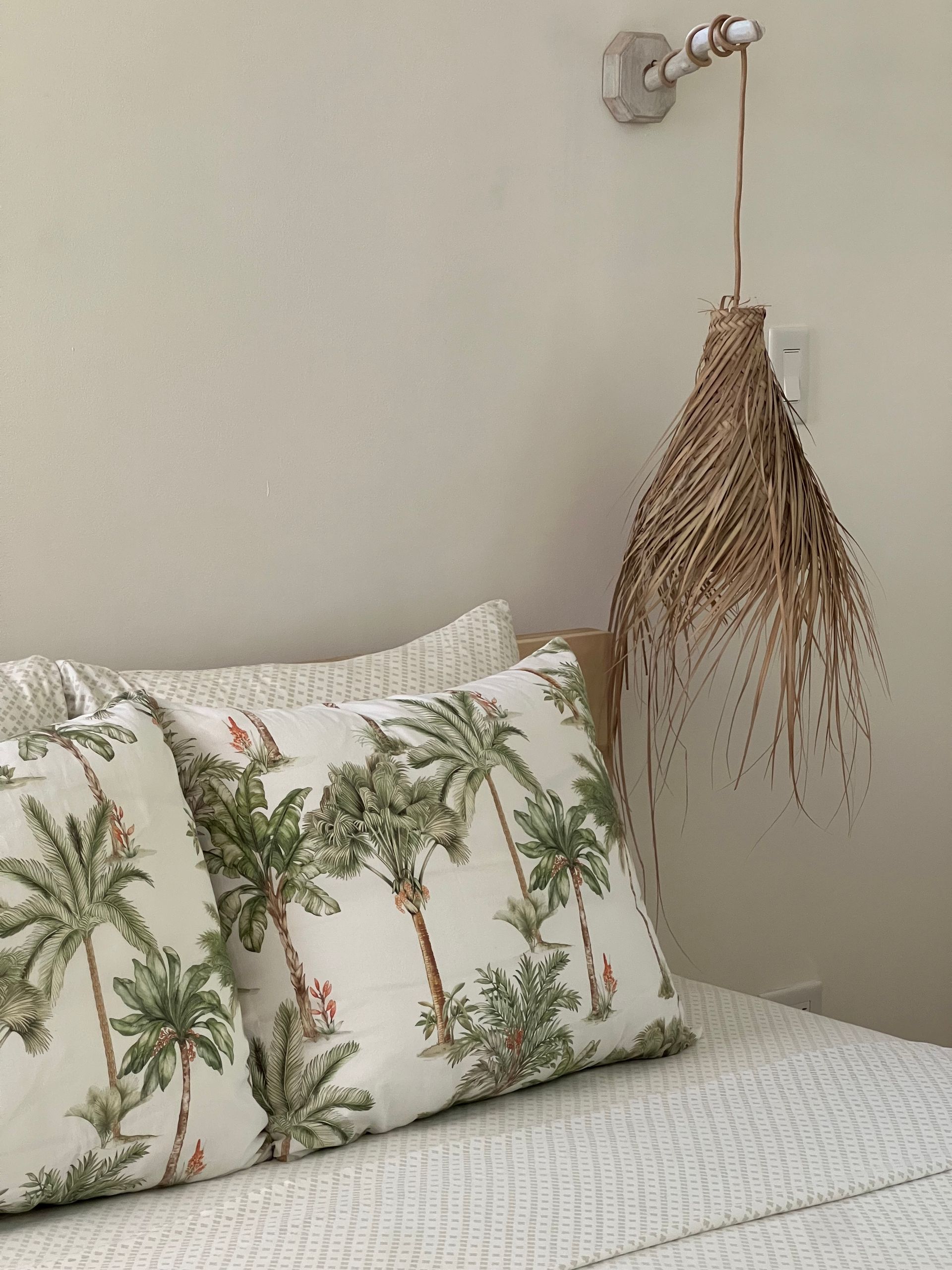 A bed with two pillows and a lamp hanging from the wall.