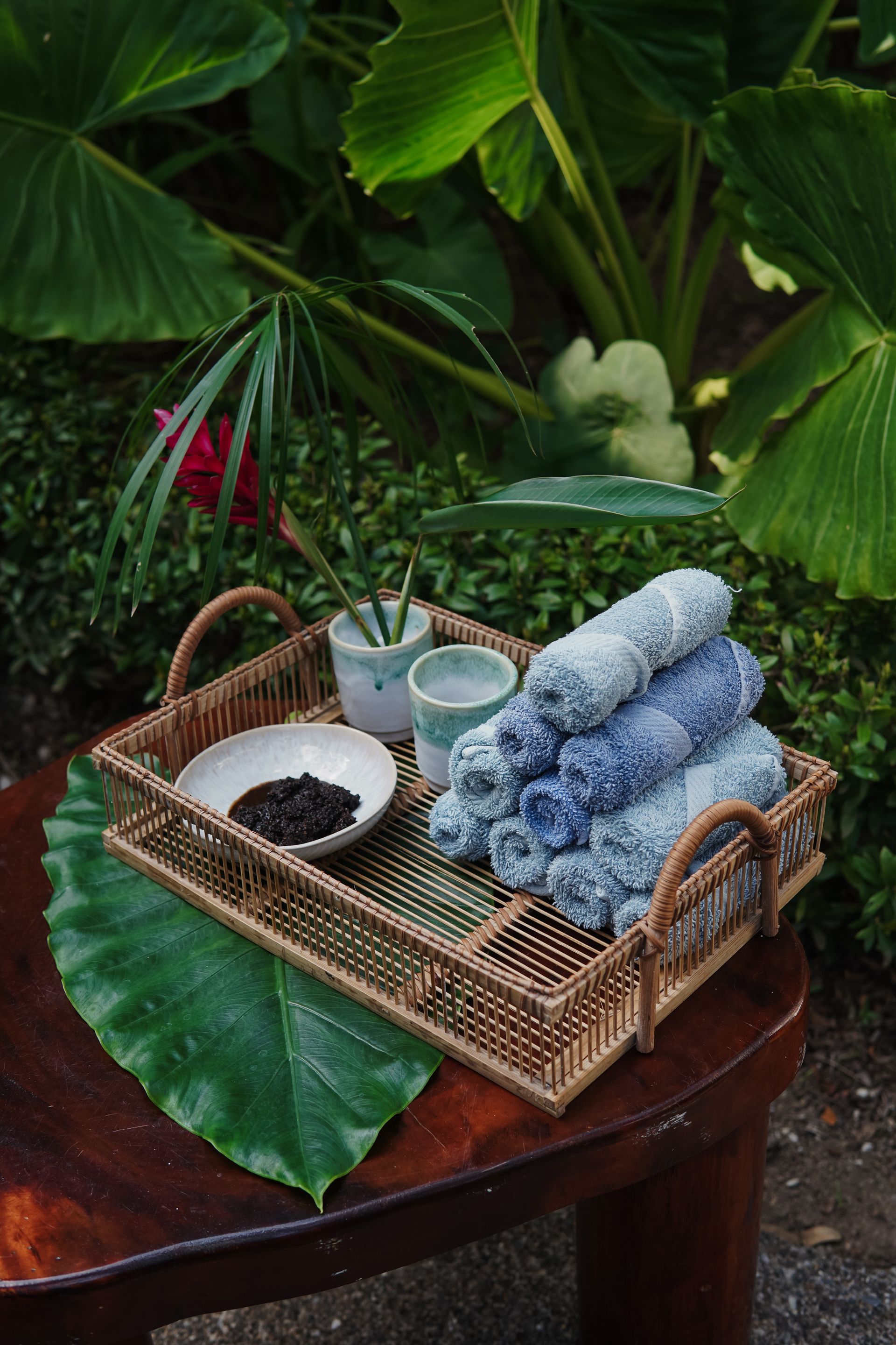 A wicker tray filled with towels , tea , and cups on a wooden table.