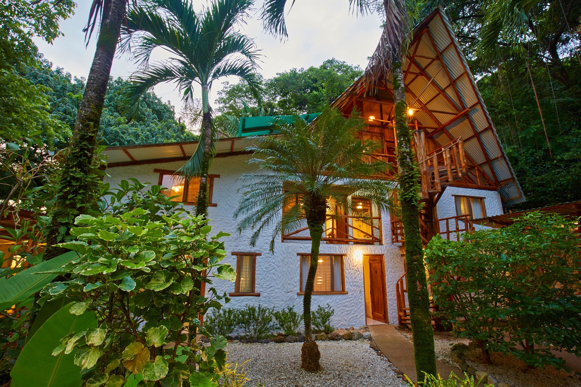 A white house with a thatched roof is surrounded by palm trees.