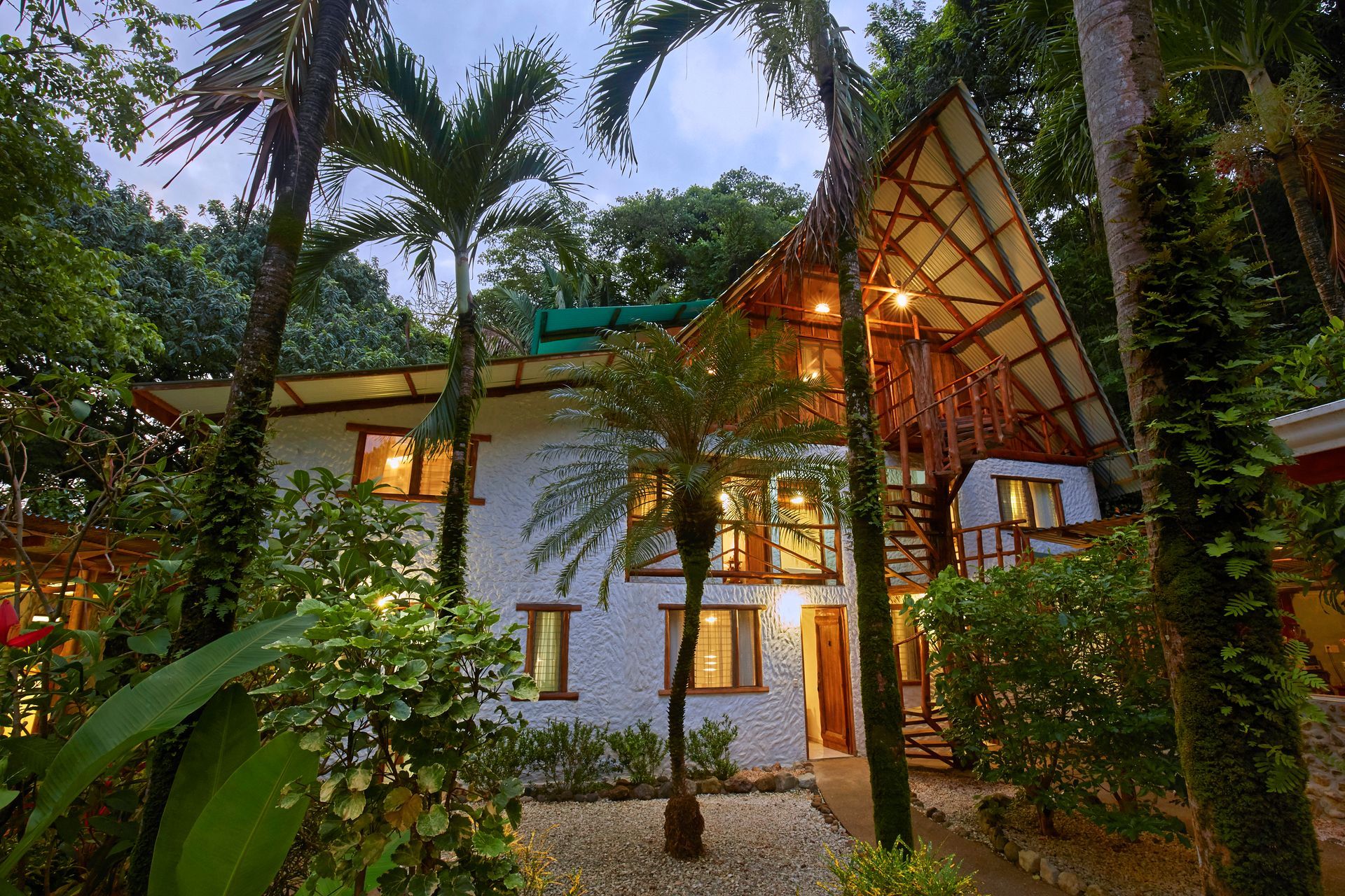 A white house with a wooden roof is surrounded by palm trees.
