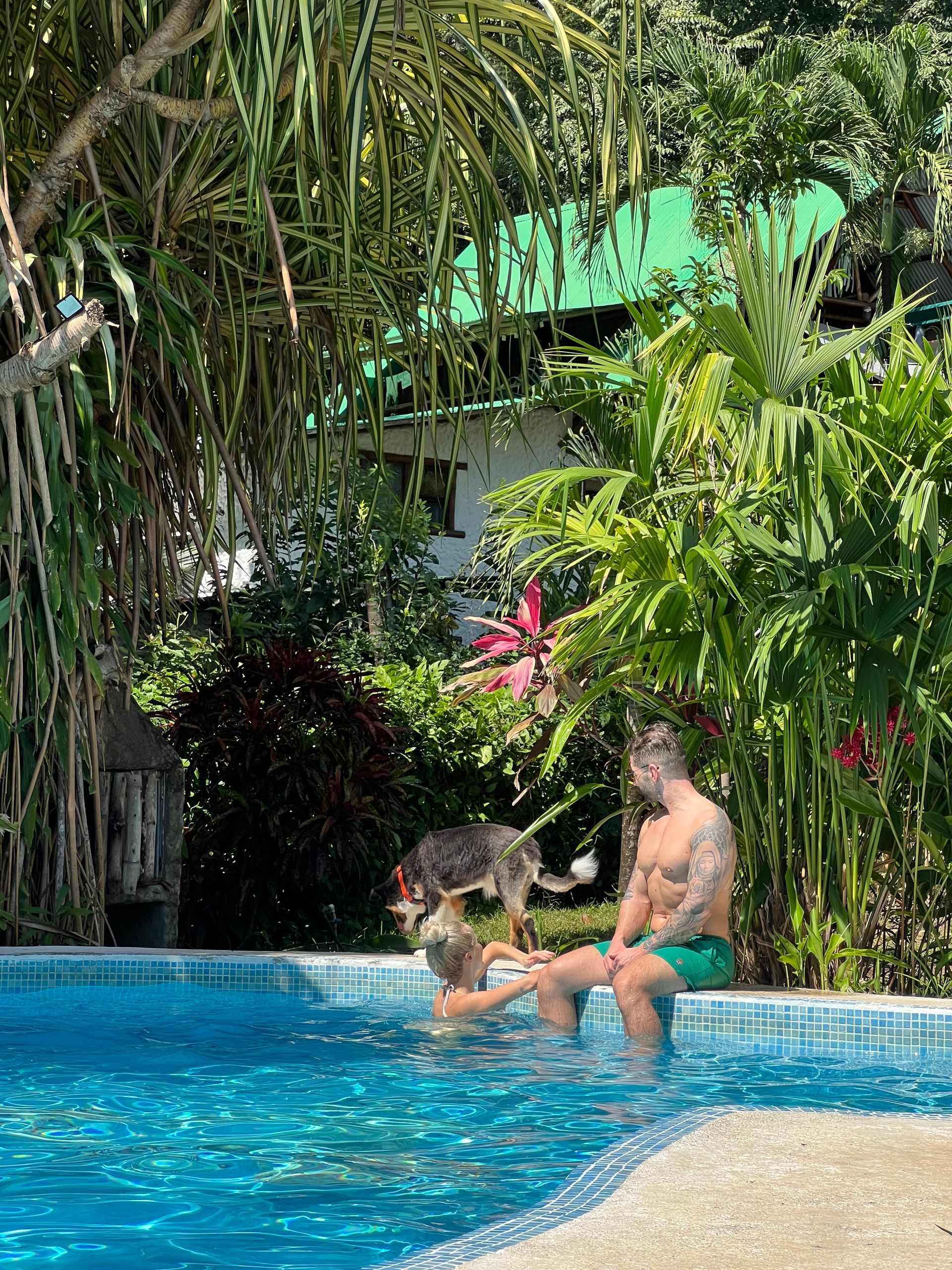 A man and a woman are sitting in a swimming pool with a dog.