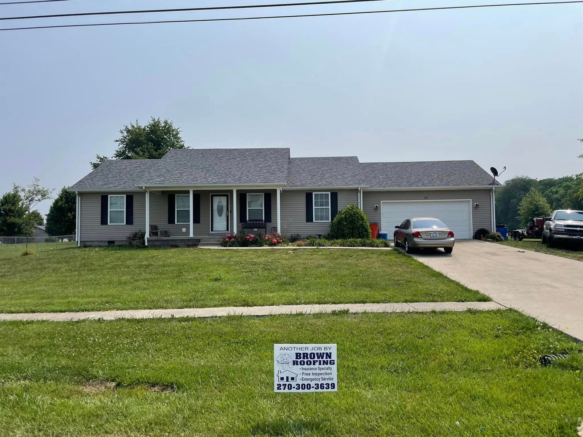 A one-story house with gray roof, green lawn, and car parked in driveway under a blue sky.