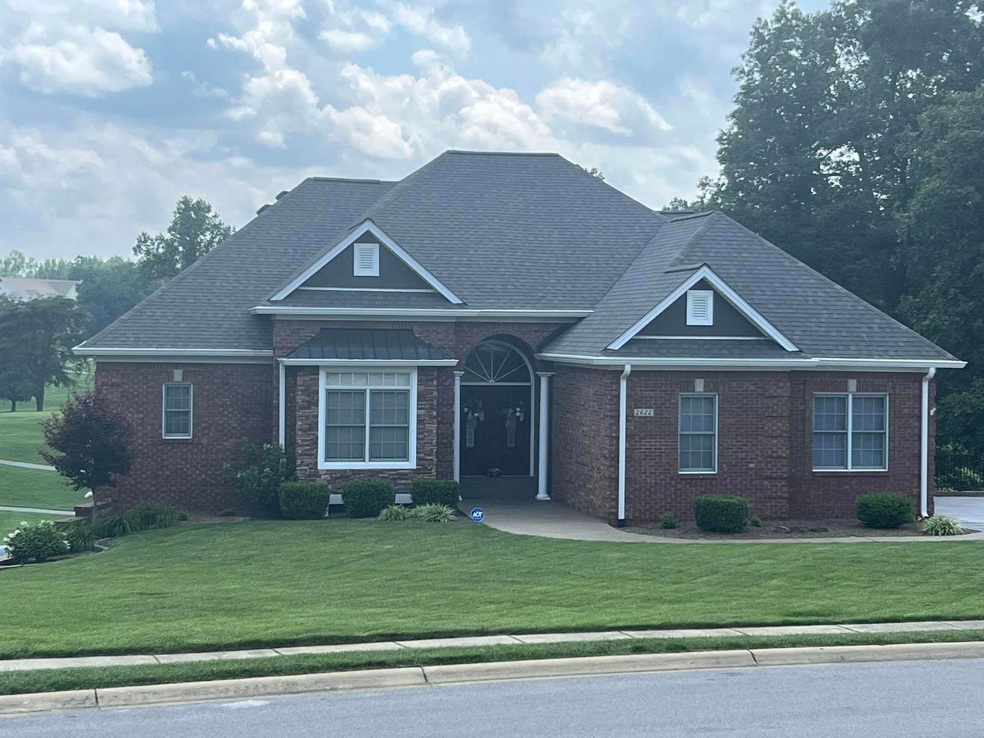 Brick house with gray roof, white trim, and a green lawn under a cloudy sky.