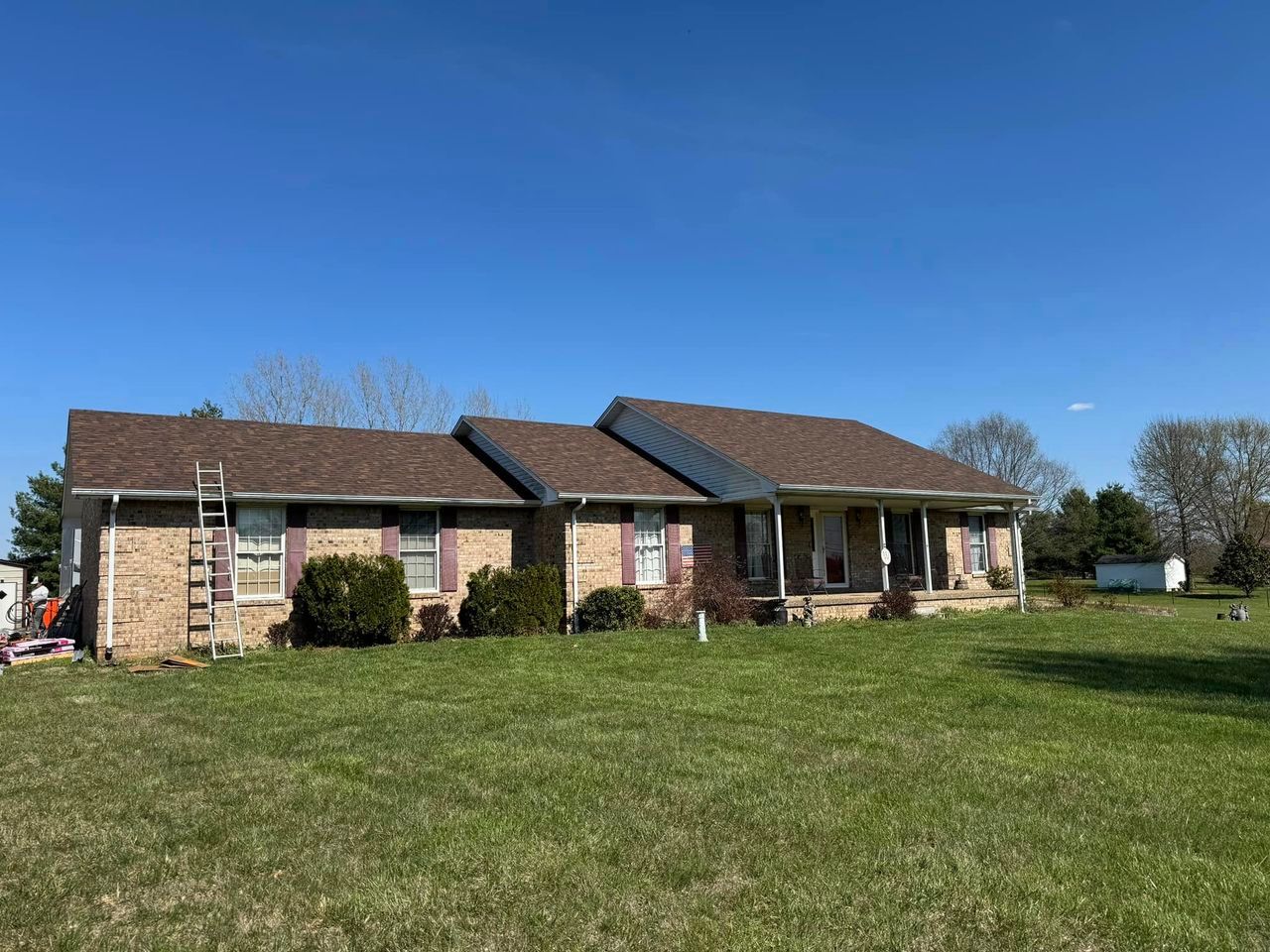 Brick ranch house with brown roof and green lawn on a sunny day.