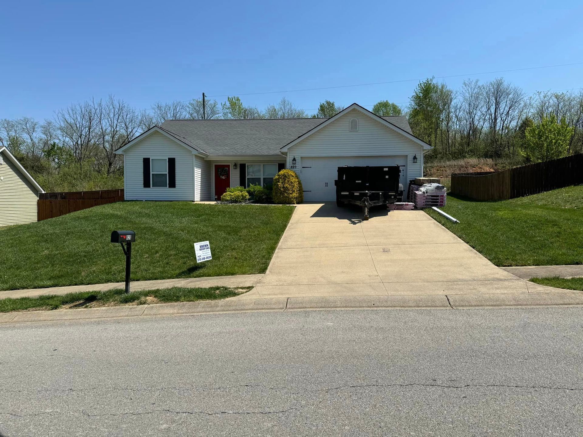 Small white house with black shutters, red front door, and a concrete driveway.