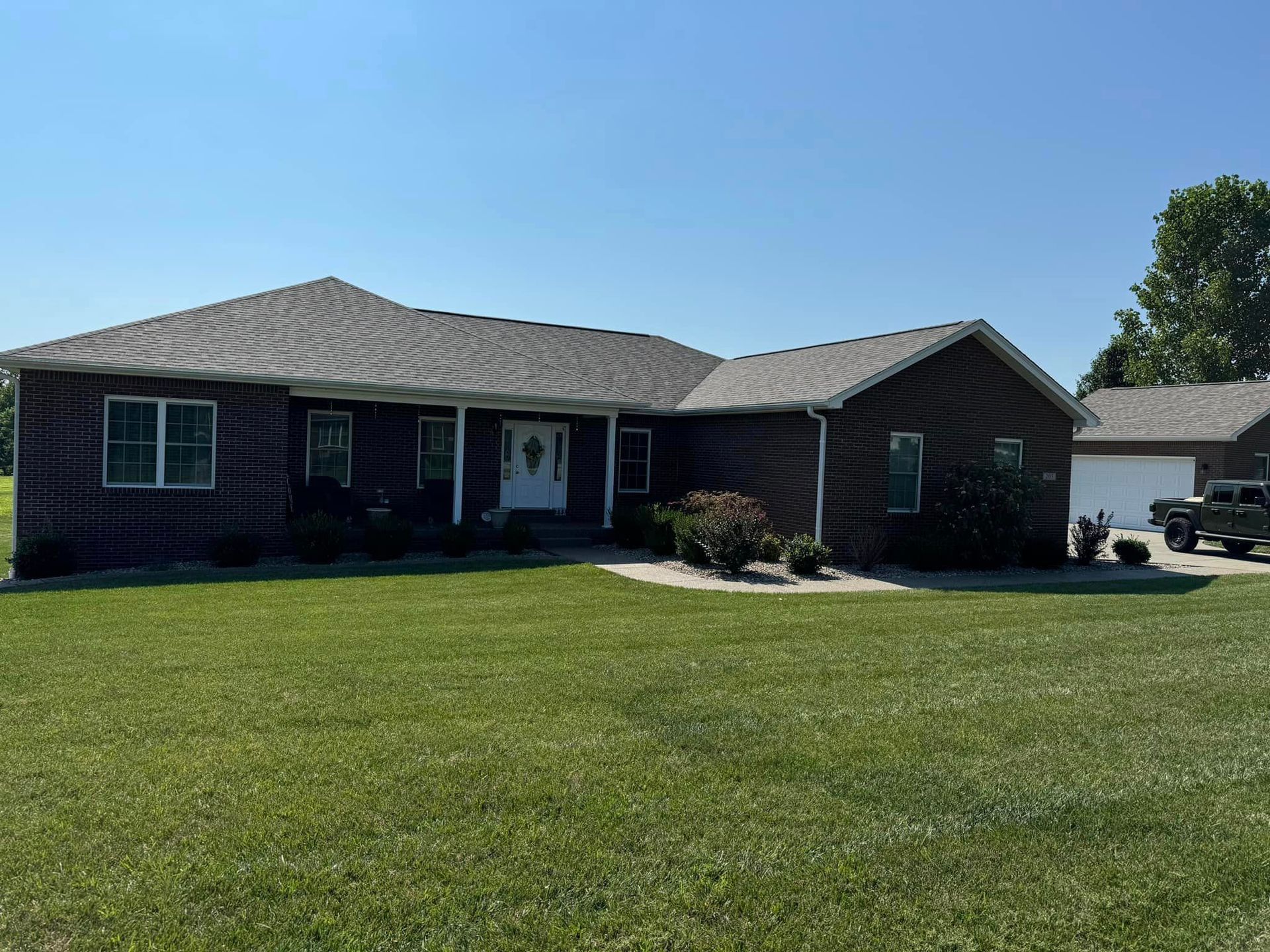 Brown brick house with green lawn under a blue sky; detached garage in the background.