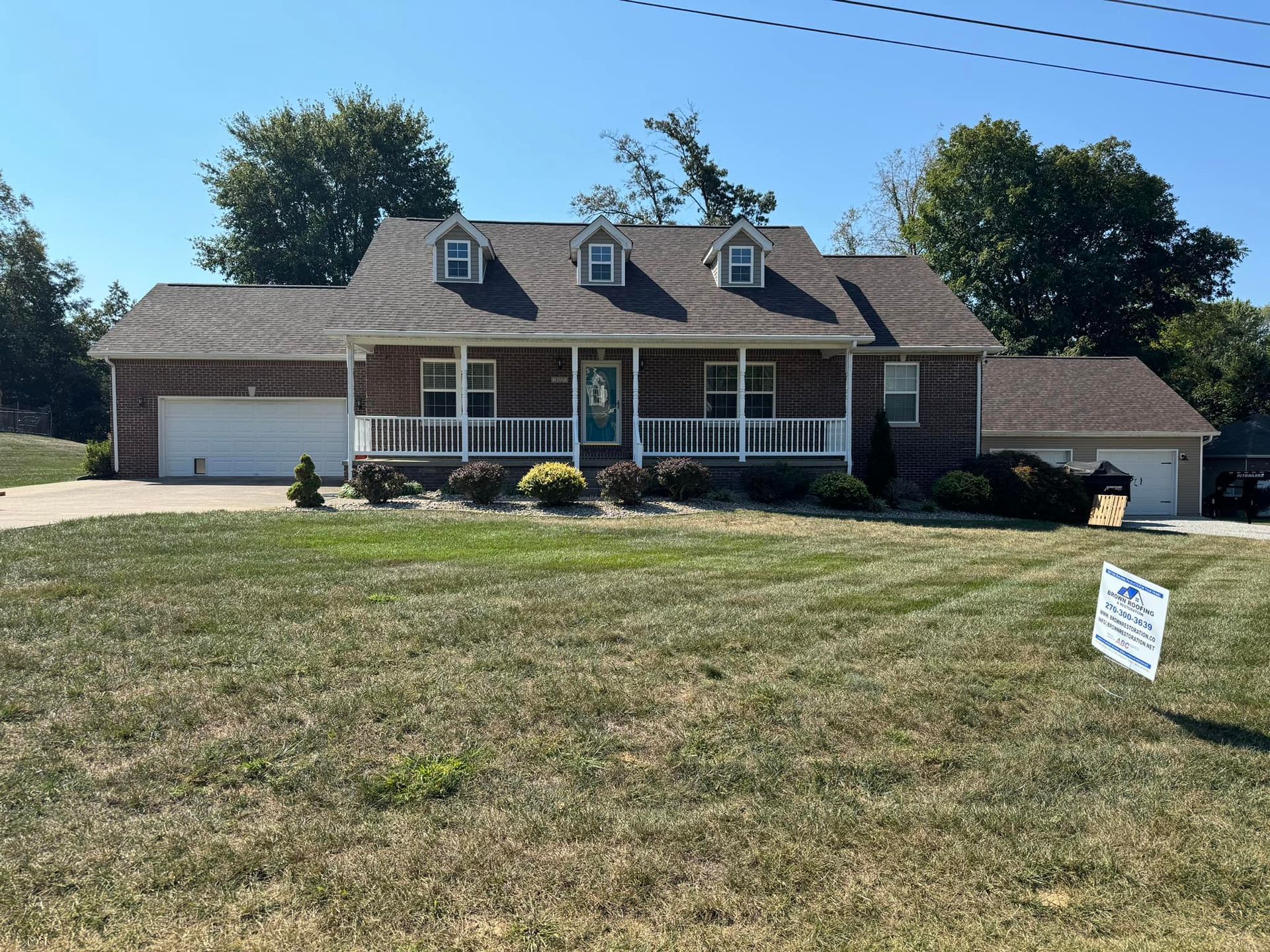 Ranch-style house with brick facade and attached garages. Features a front porch and dormer windows, set on a grassy lawn.