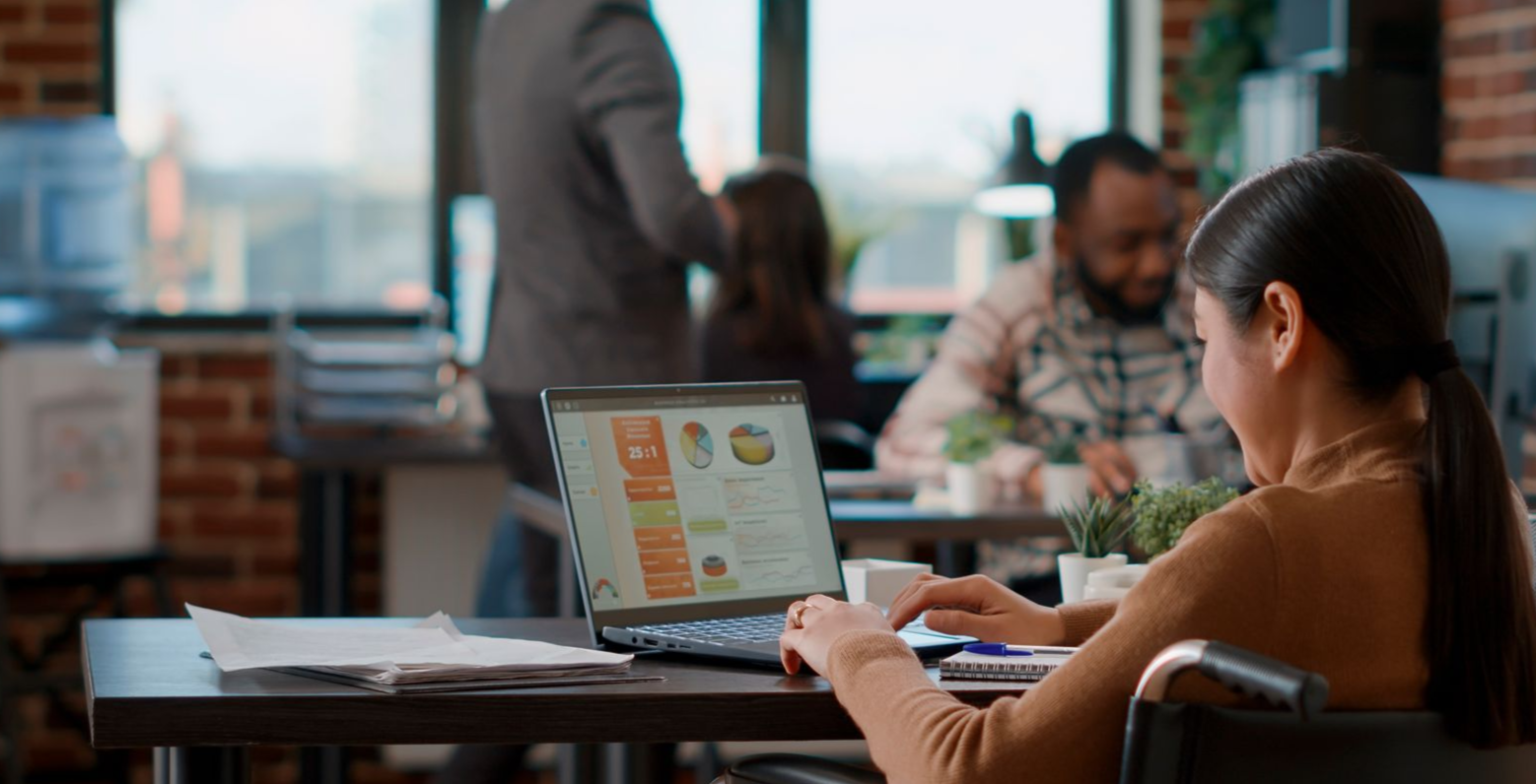 Woman in a wheelchair working on a laptop at a desk in an office setting.