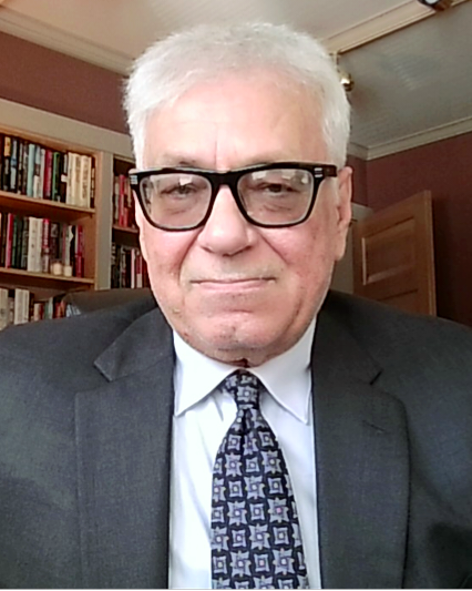 Man in suit and glasses, smiling slightly, in front of a bookshelf.