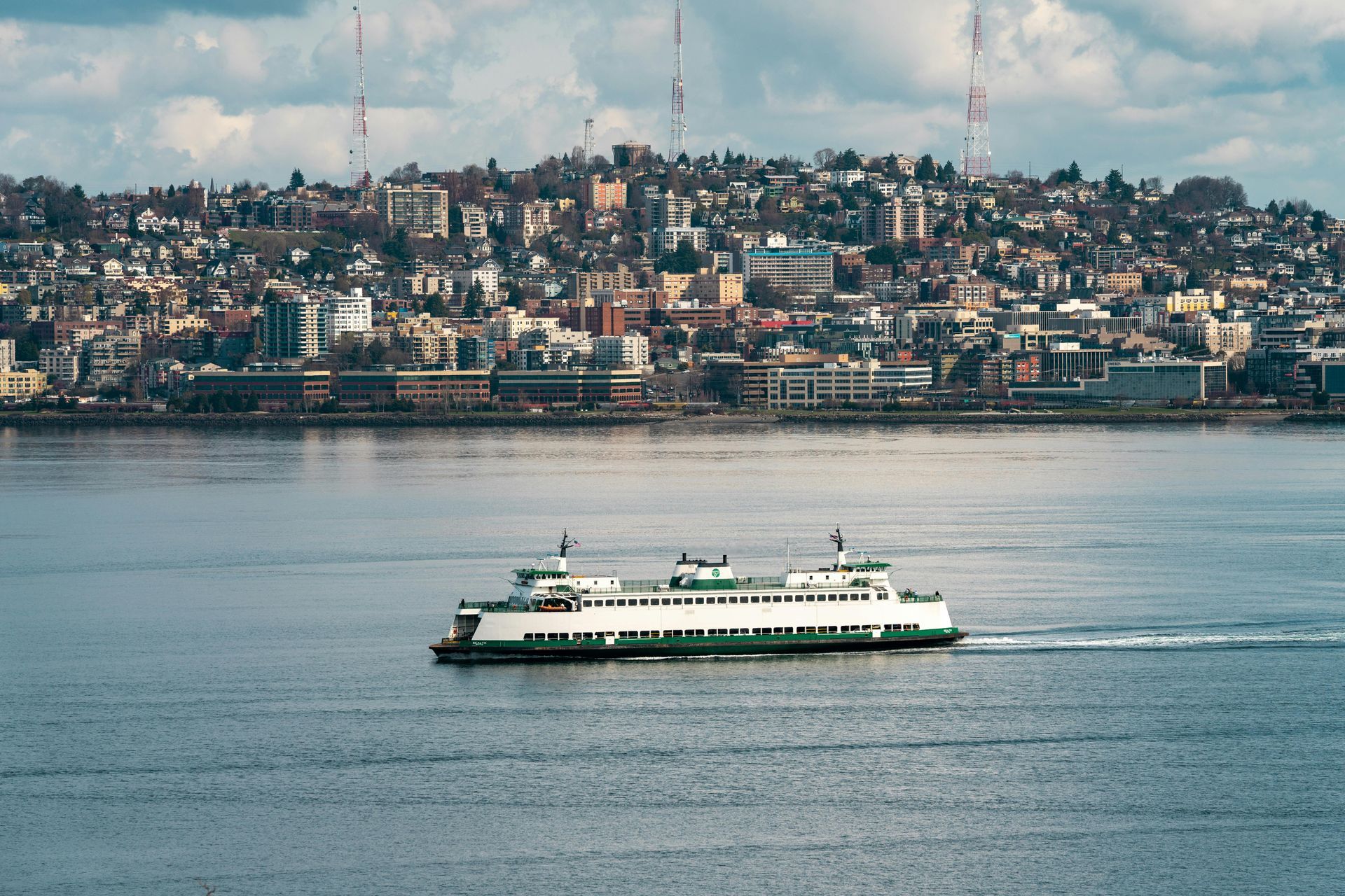 Ferry boat sailing across water with city skyline in the background. Green and white ferry.