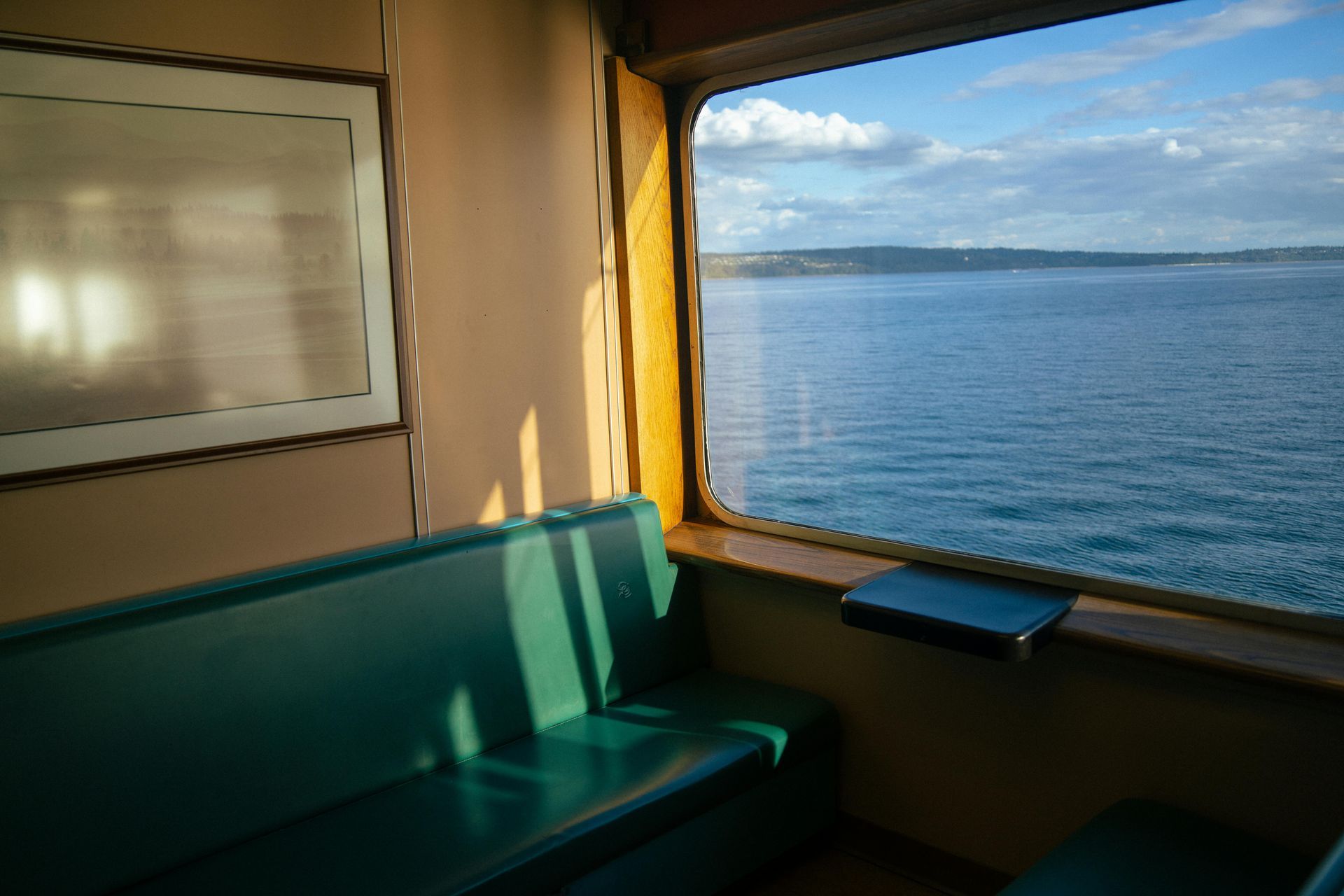 Interior of a boat with a teal bench seat and a window overlooking a calm blue sea under a sunny sky.