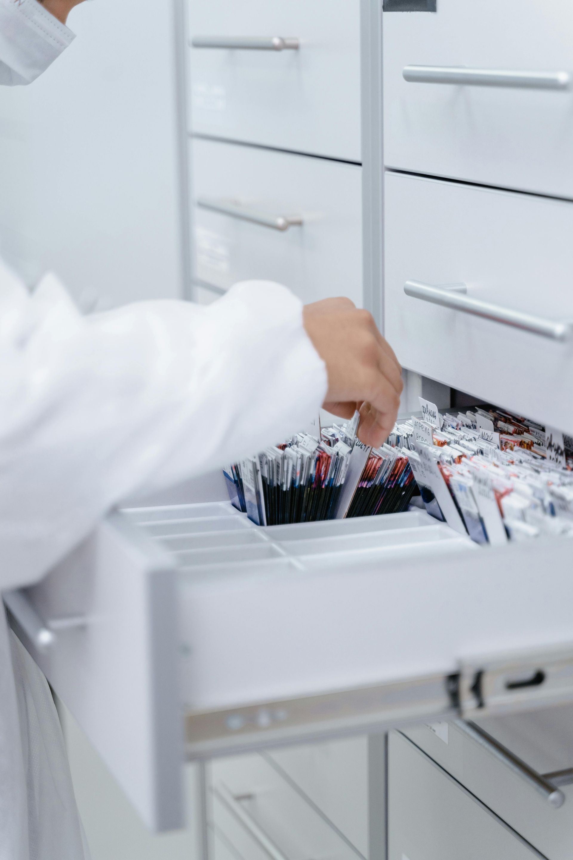 Person in lab coat reaching into a drawer filled with vials in a bright, white room.