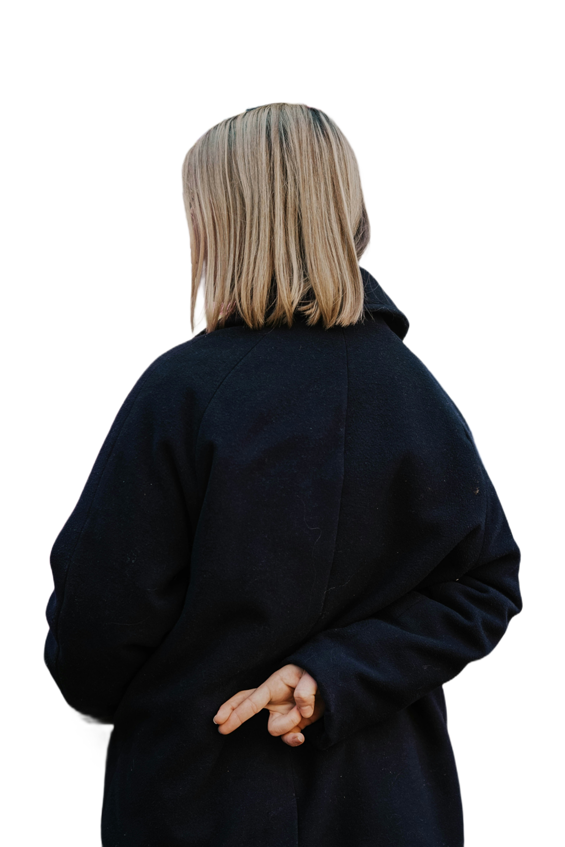 Person with blonde braids, back to the camera, wearing a dark coat, fingers crossed behind their back.