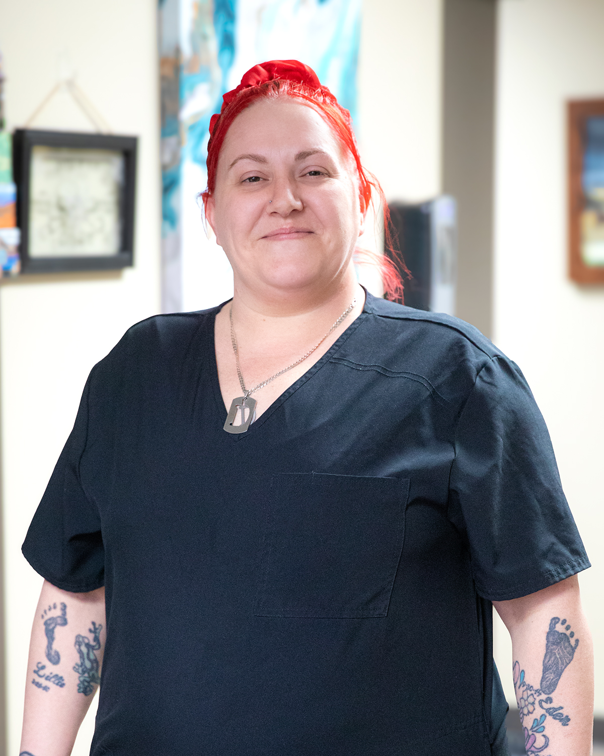 A woman with red hair and tattoos is wearing a black scrub top.