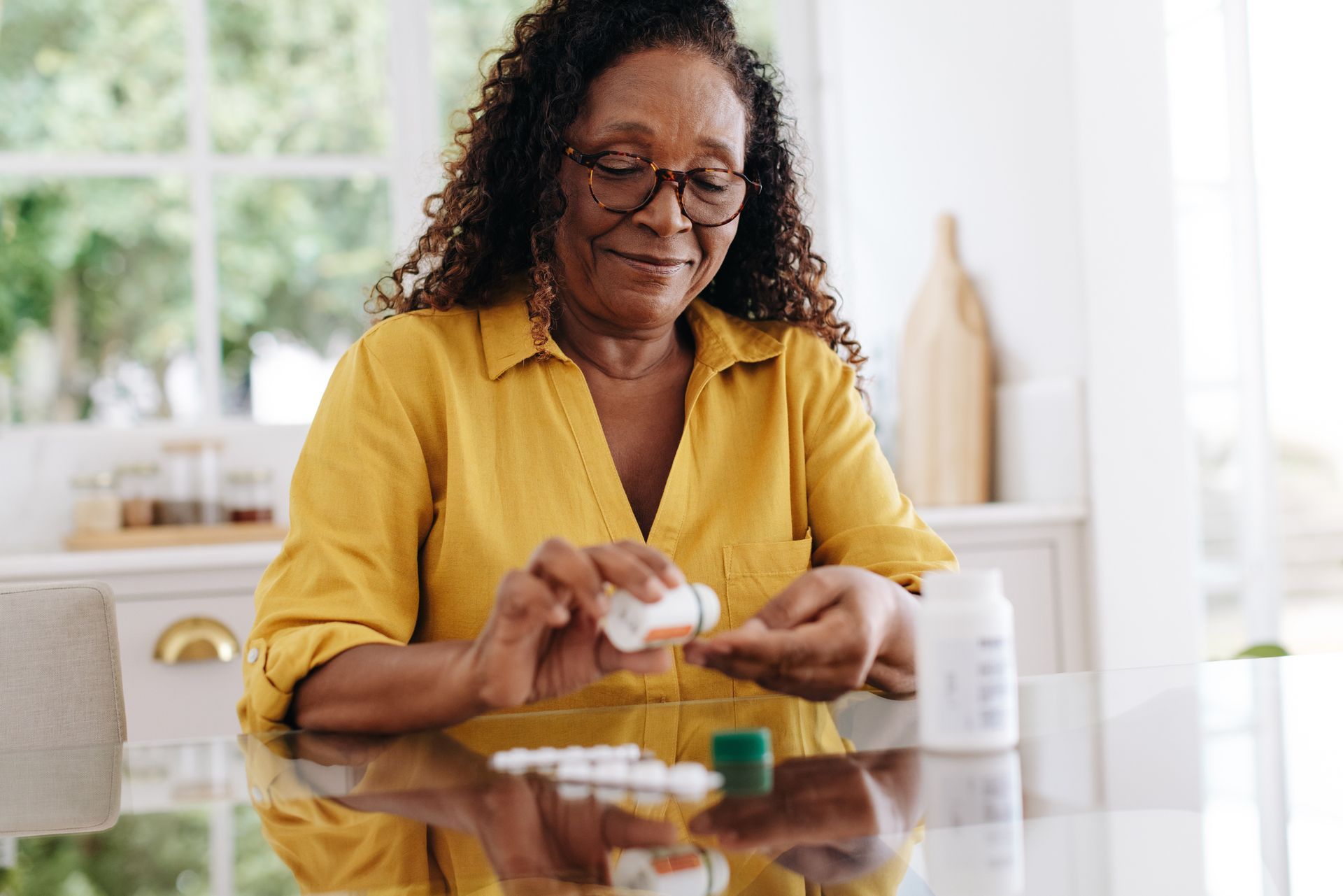 Woman in yellow shirt taking pills at a kitchen table, smiling.