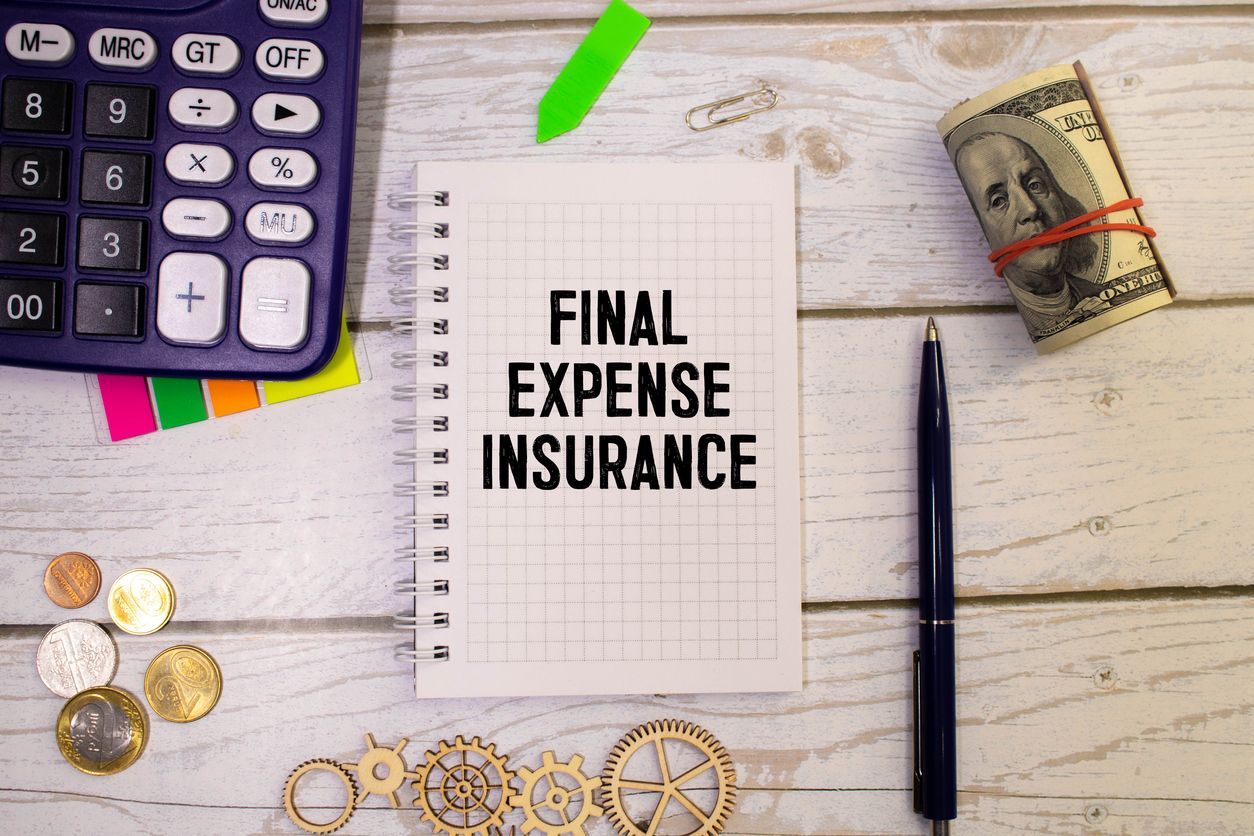 Expense insurance note beside calculator, pen, coins, and rolled cash on a white desk.