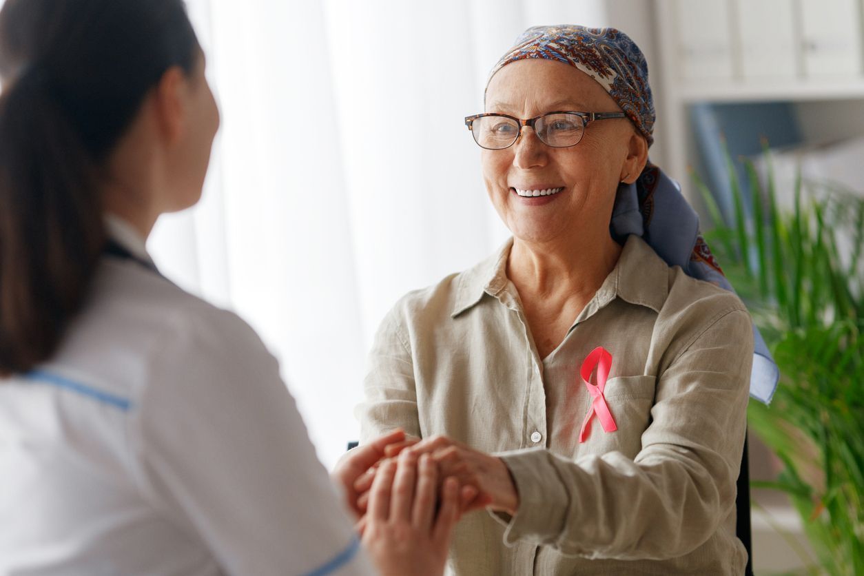 Doctor and patient with cancer ribbon, holding hands and smiling.