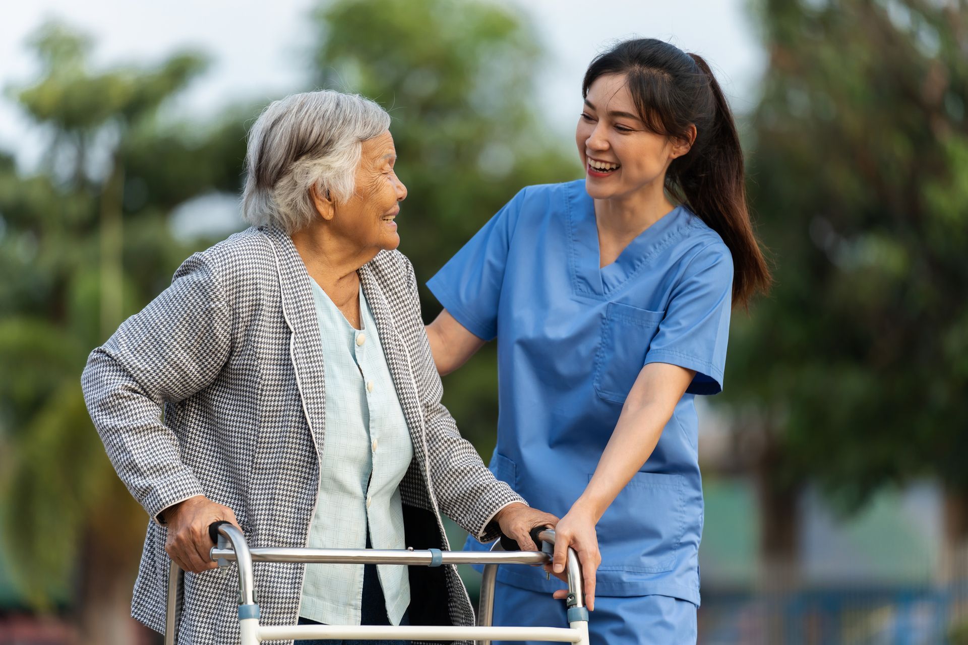 Smiling caregiver assisting an elderly woman using a walker outdoors.