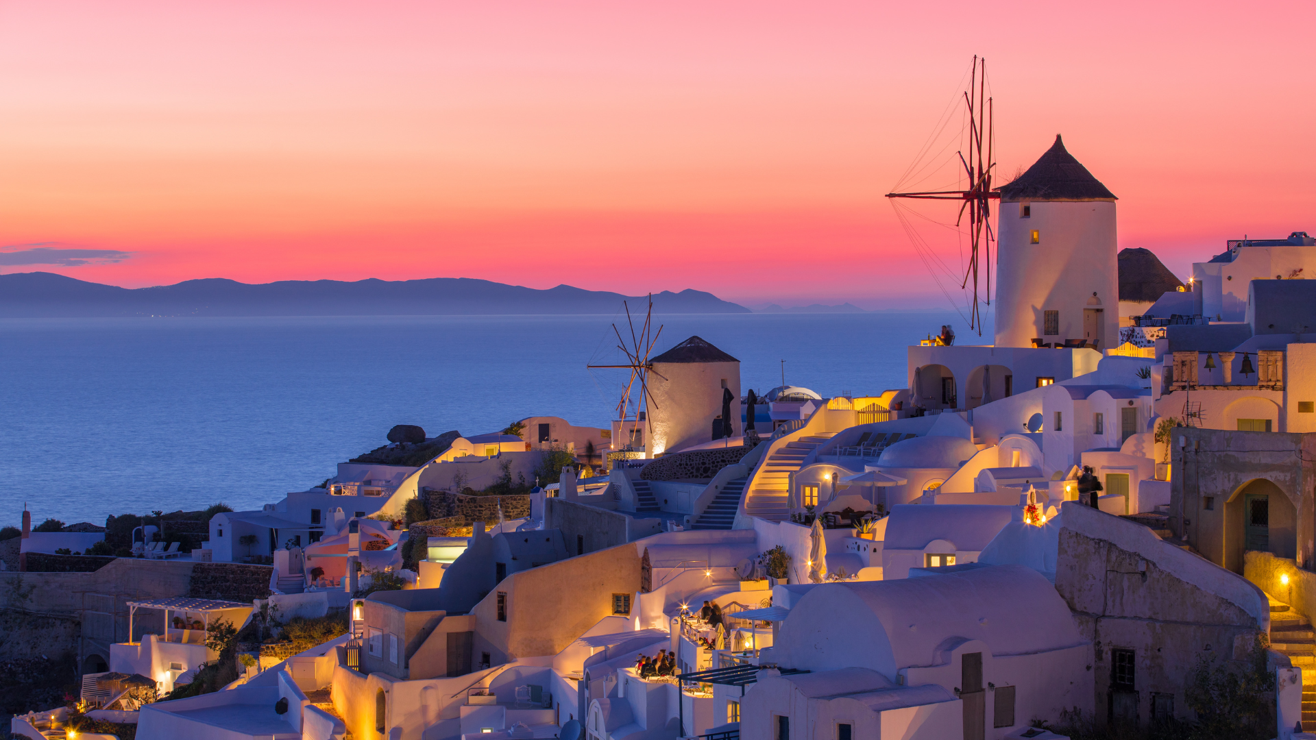 The windmills are lit up at night and there is a sunset in the background.