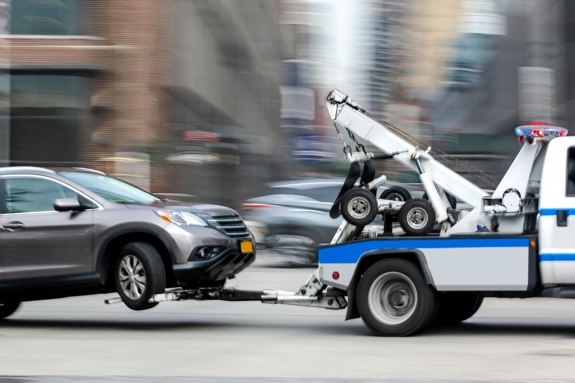 Tow truck towing a silver SUV on a city street with motion blur.
