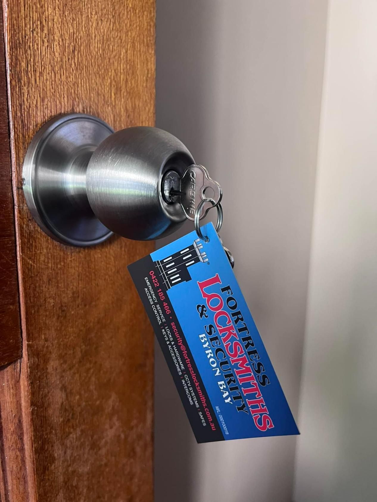 A Door Knob with A Business Card Attached to It — Fortress Locksmiths & Security in Lennox Head, NSW