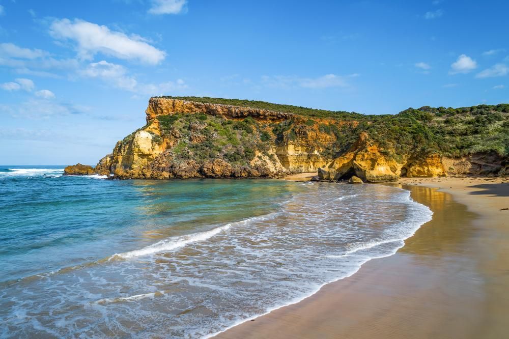 A Beach with A Cliff in The Background and Waves Crashing on The Sand — Fortress Locksmiths & Security in Ocean Shores, NSW