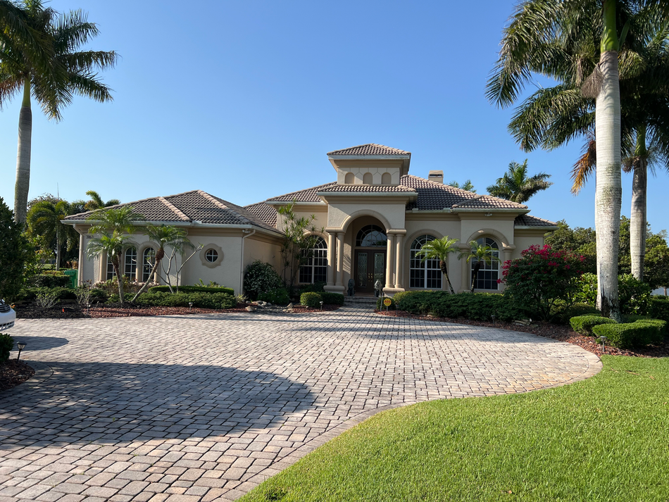 Lord of homes with brick, long driveway, clear skies, palm trees, and green grass.