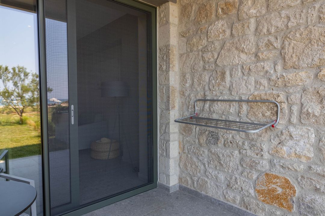 Porta scorrevole in vetro con zanzariera e parete in pietra con stendino su un balcone.
