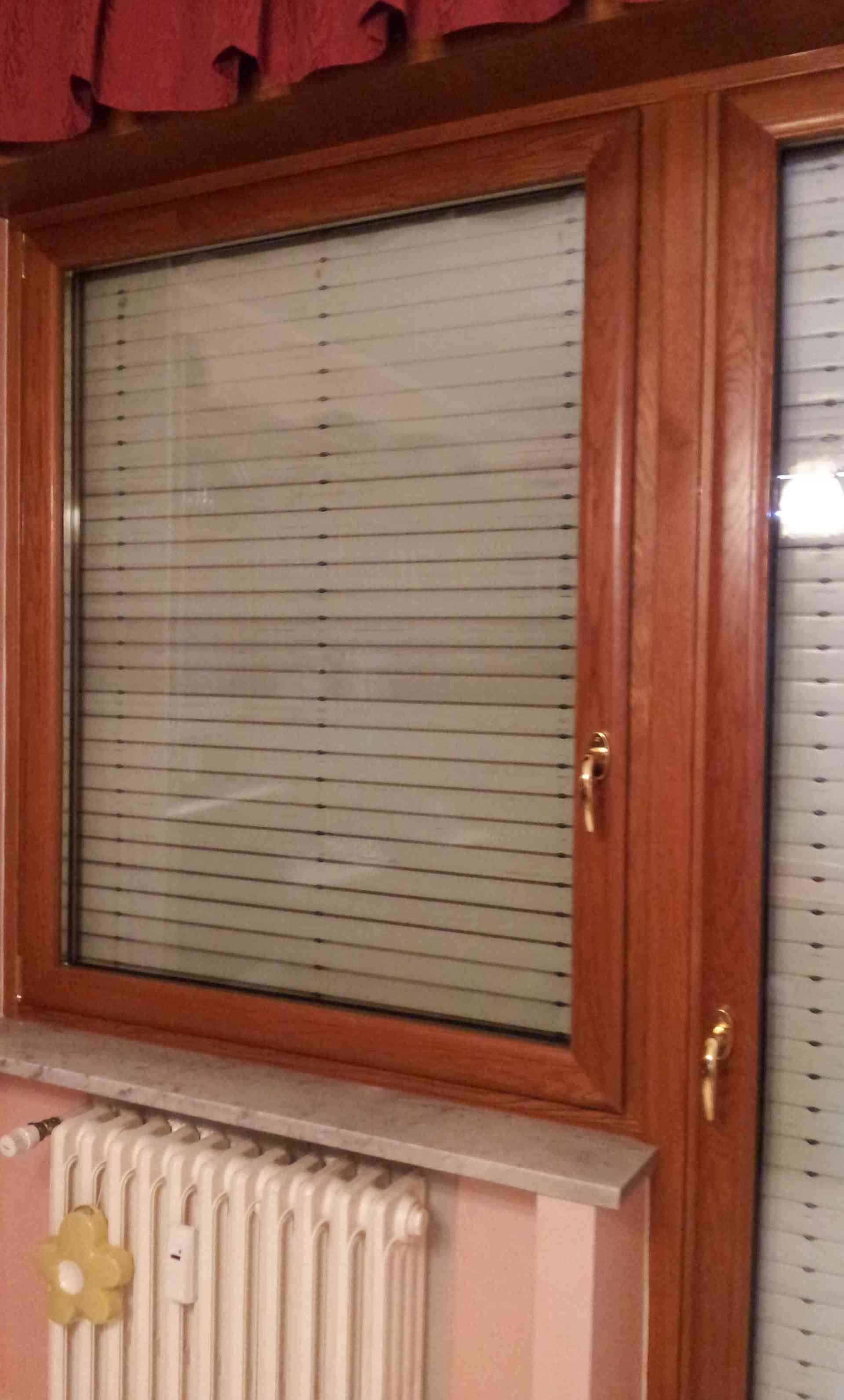 Finestra in legno marrone con persiane, sopra un termosifone, in una stanza con pareti rosa.