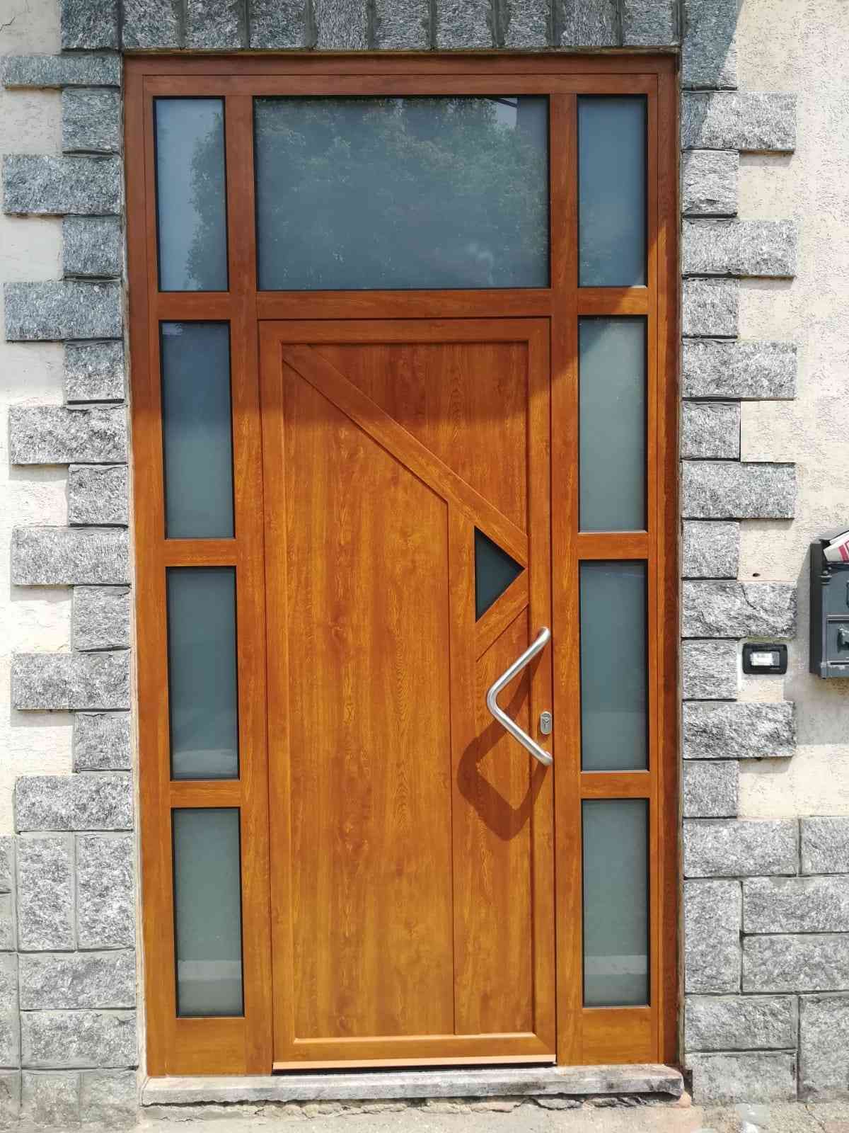 Porta d'ingresso in legno con vetri laterali e sopraluce, incastonata in una facciata in pietra.
