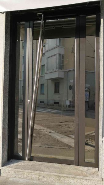 Porta in vetro con un palo di metallo appoggiato, che riflette una scena di strada.