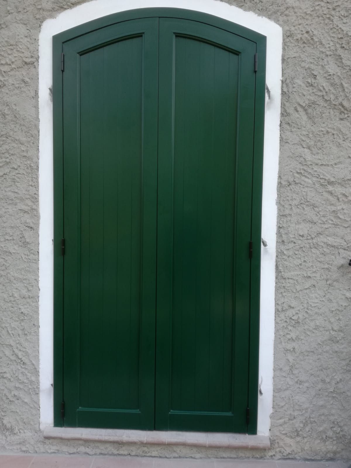 Persiane verdi su una parete in stucco, delineate da una rifinitura bianca.