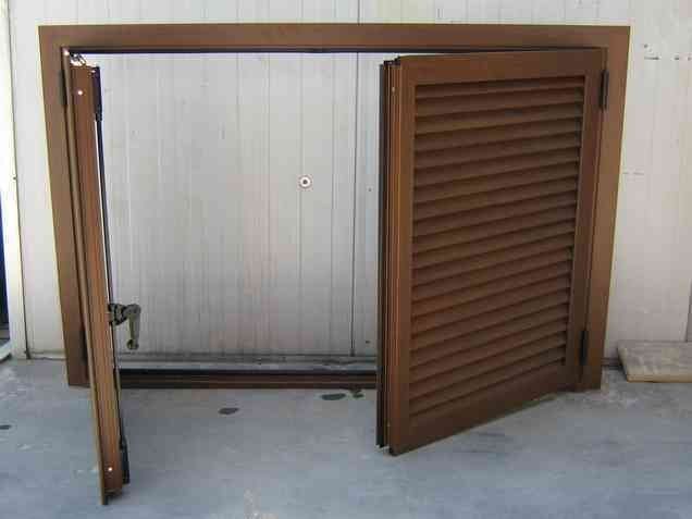 Delle persiane marroni, parzialmente aperte, si trovano di fronte a una parete con doghe bianche, incastonata in una cornice marrone.