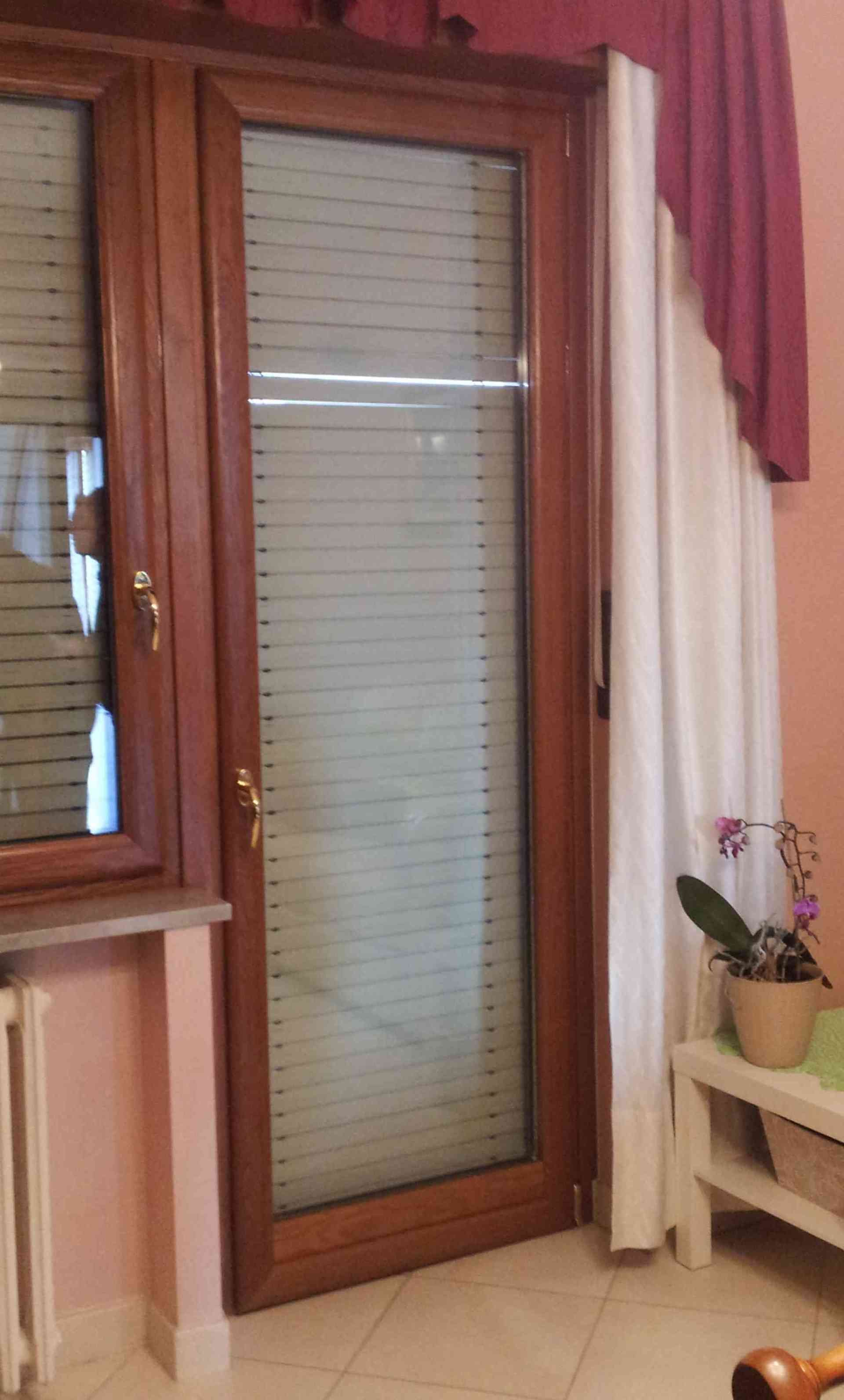 Porta in legno con vetro smerigliato e tenda bianca. Una piccola pianta in vaso è appoggiata su un tavolo bianco lì vicino.