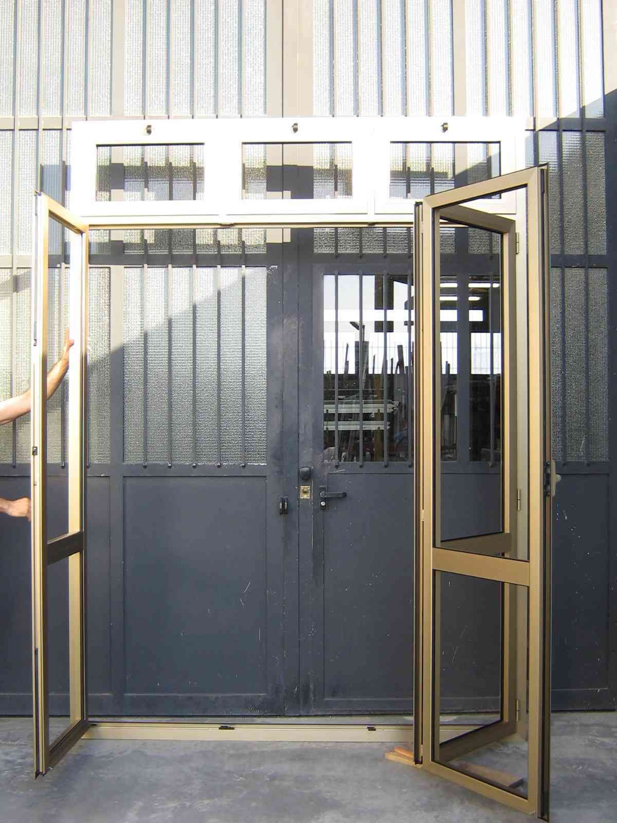 Telaio di una porta in alluminio aperto appoggiato a una porta in metallo grigio scuro con pannelli in vetro e una piccola finestra sopra.