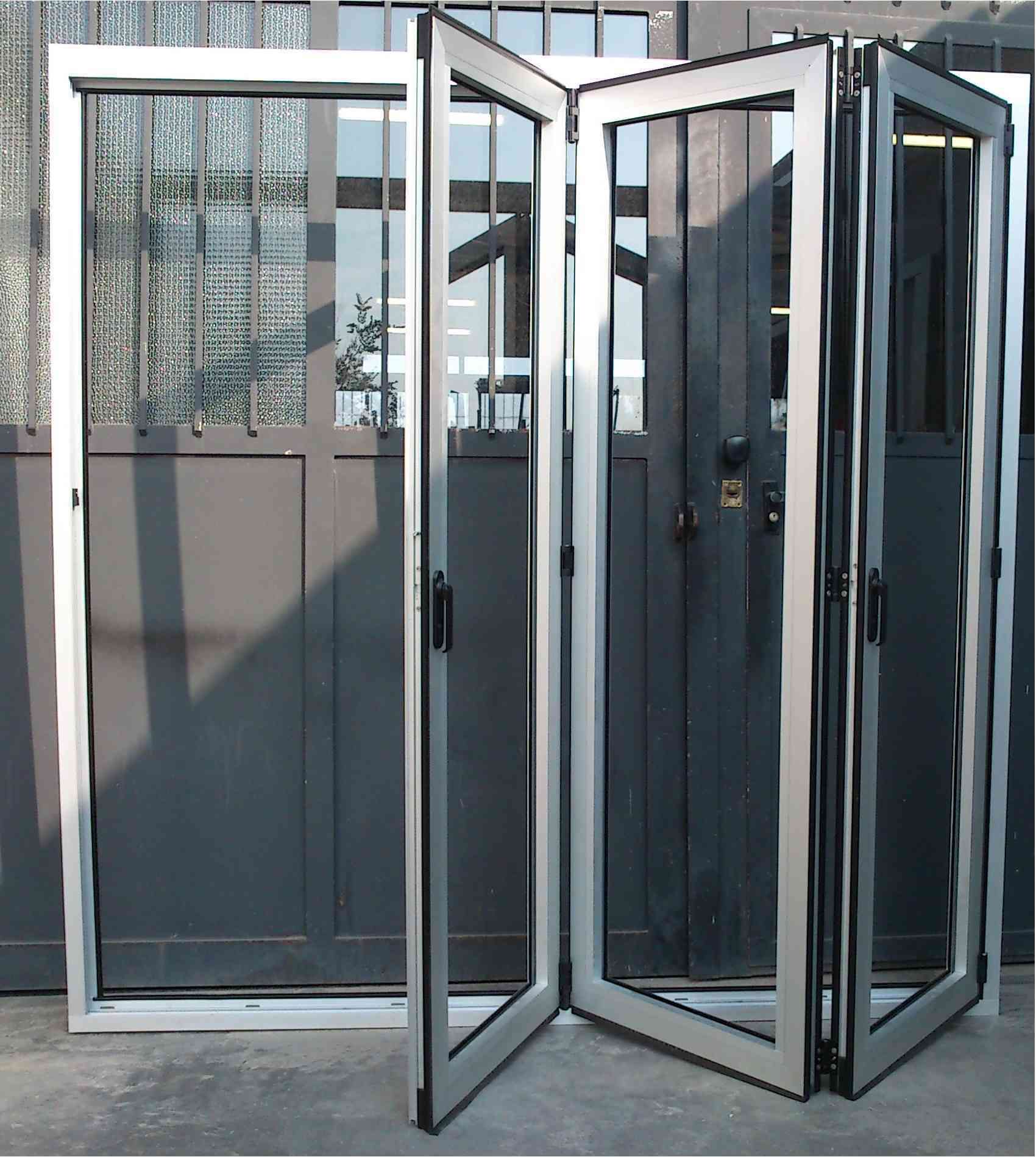 Porta a soffietto in vetro con cornici argentate, parzialmente aperta, su sfondo grigio.