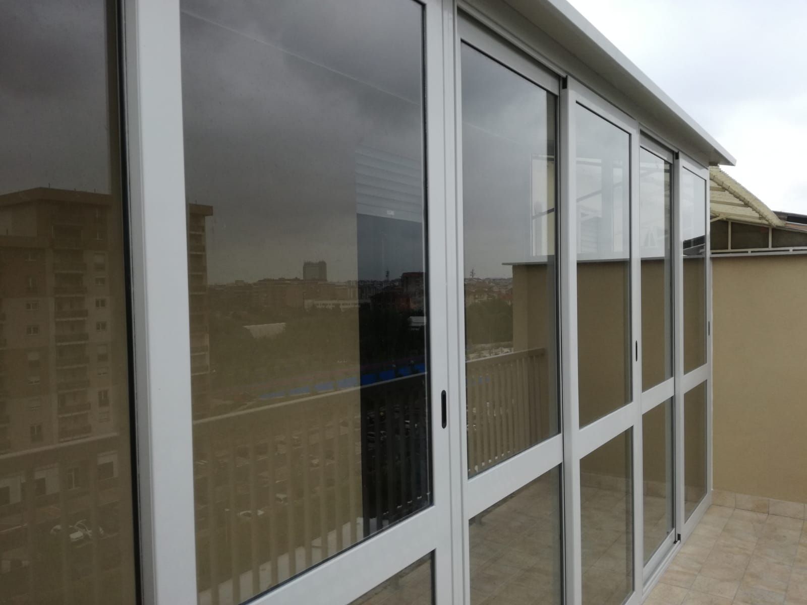 Balcone con vetrate e cornici bianche, con vista sulla città in una giornata nuvolosa.