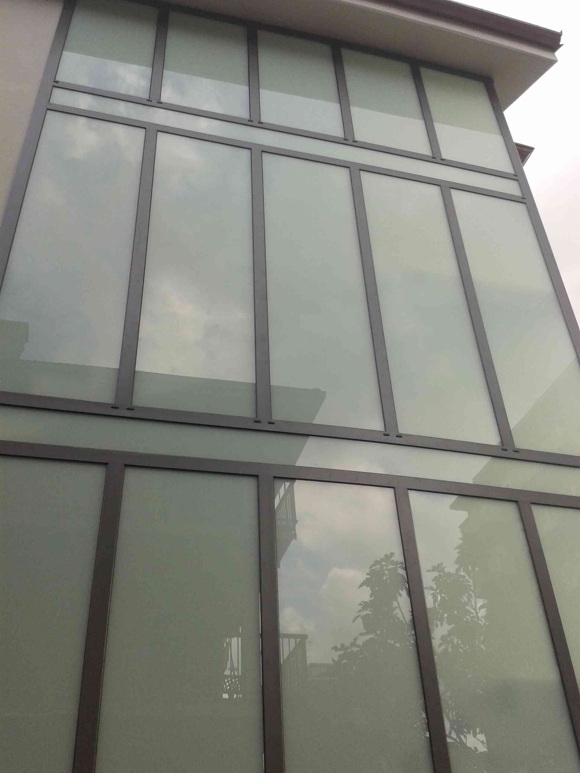 Esterno di un edificio alto con grandi finestre rettangolari che riflettono il cielo e gli alberi.