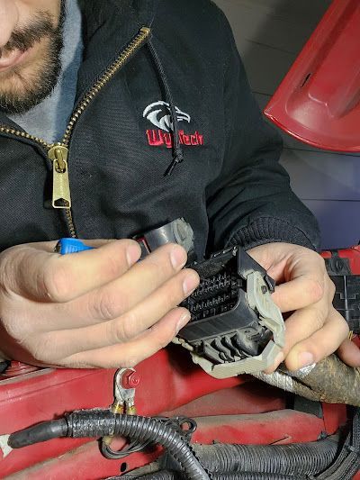 A man wearing a black jacket that says way tech is working on a car