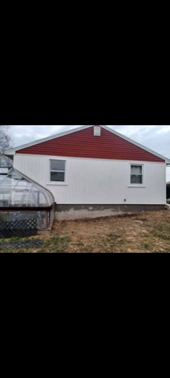 A white house with a red roof and a greenhouse in the backyard.