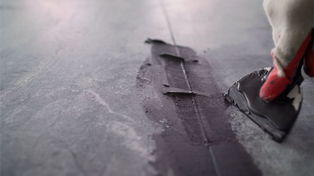 A person is using a spatula to spread cement on a tile floor.
