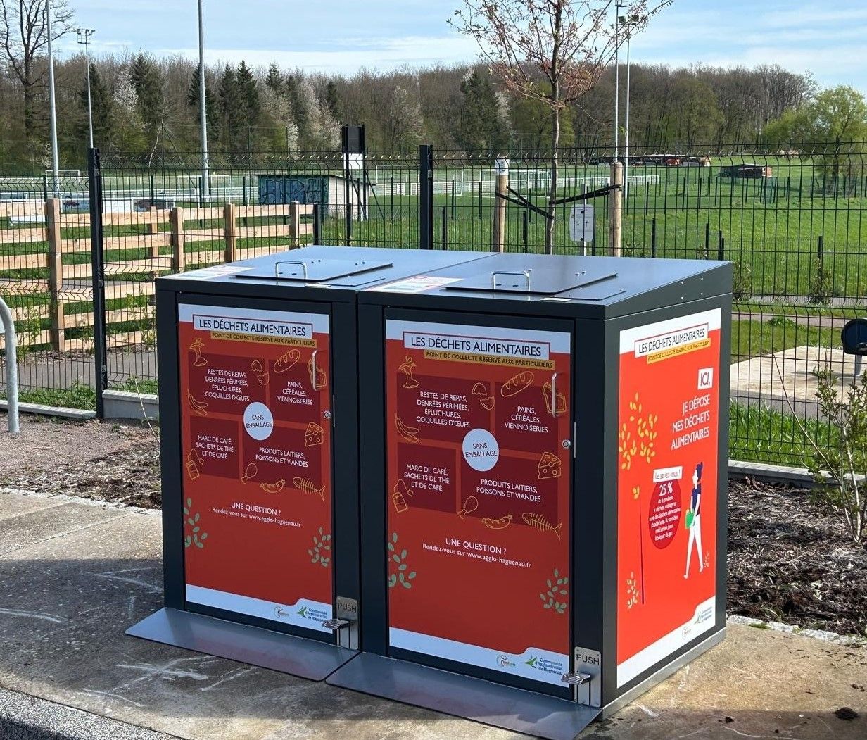 Deux poubelles avec des affiches rouges et blanches, dans un parc.
