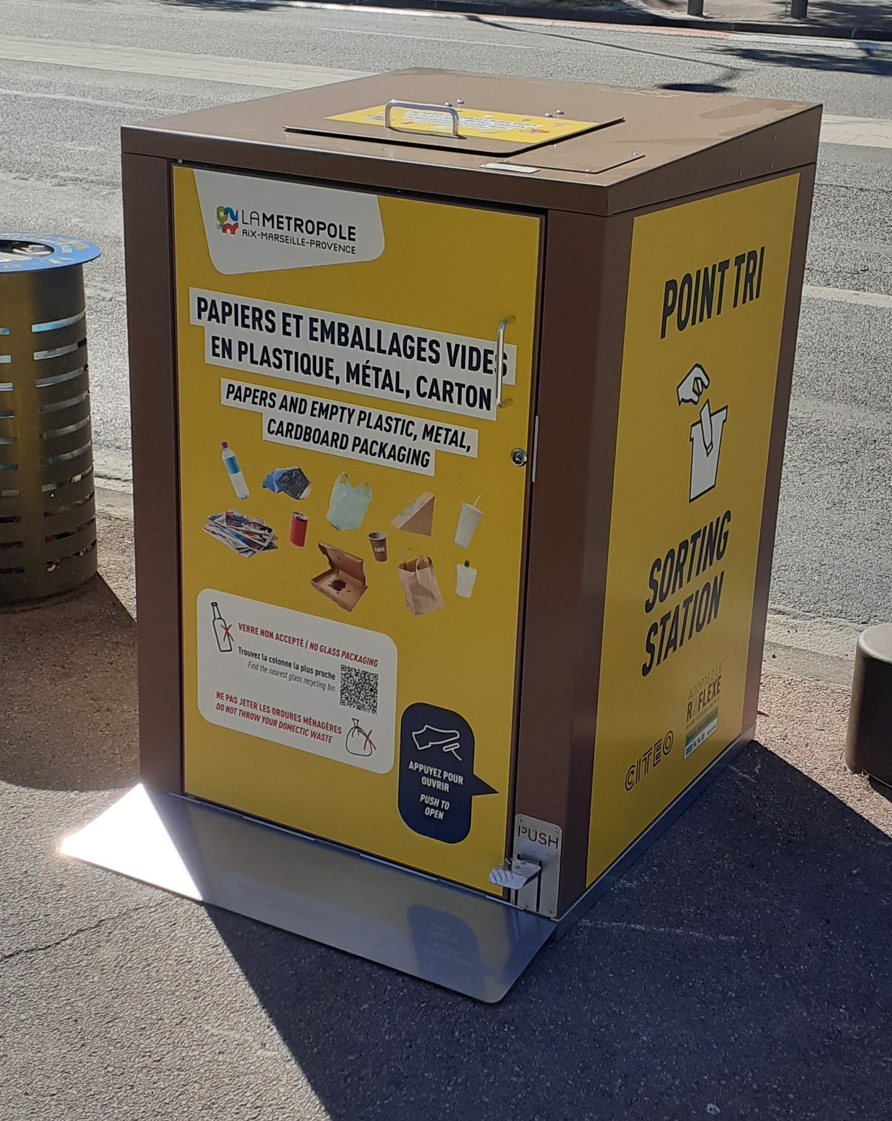 Bac de recyclage jaune pour le papier, le plastique, le métal et le carton par une journée ensoleillée.