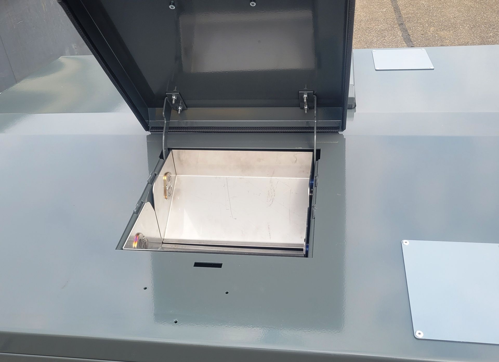 Boîte métallique grise ouverte avec couvercle à charnière, révélant un intérieur argenté.